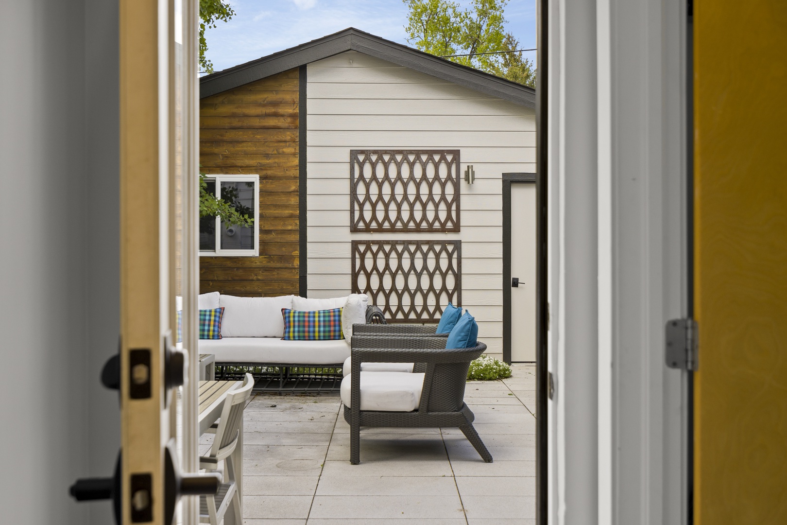 Step through French doors onto your private patio, where comfortable outdoor seating awaits beneath blue skies.