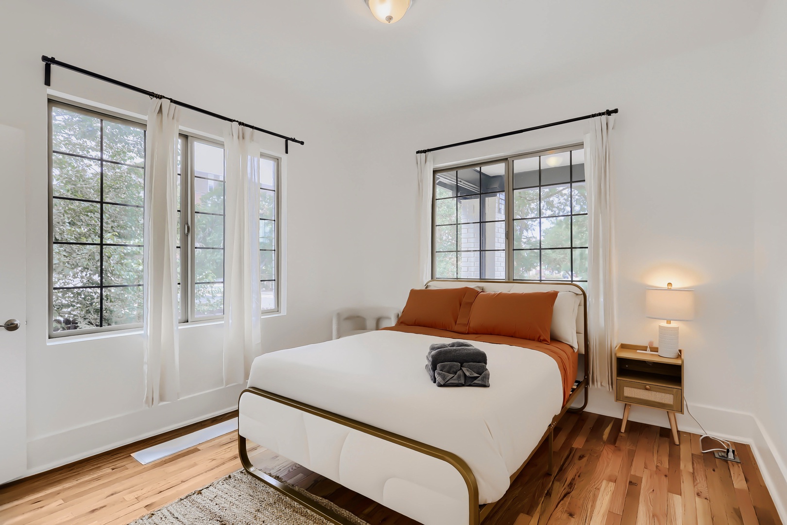Step into your serene retreat with warm wood floors, crisp white linens, and windows that frame peaceful treetop views—your perfect space to unwind.