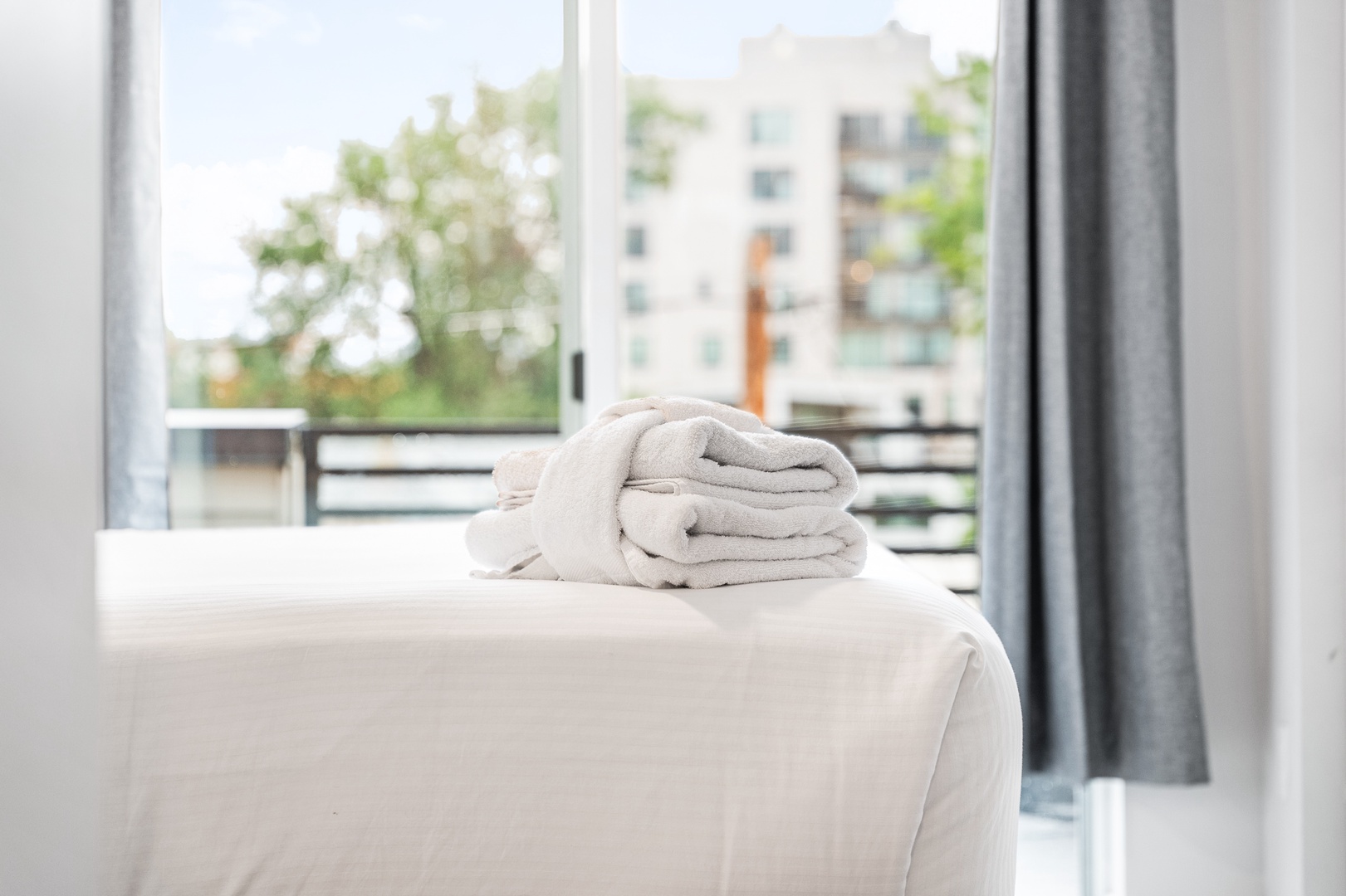 Crisp linens and plush towels await you in this light-filled bedroom, where balcony doors frame leafy trees and city views.