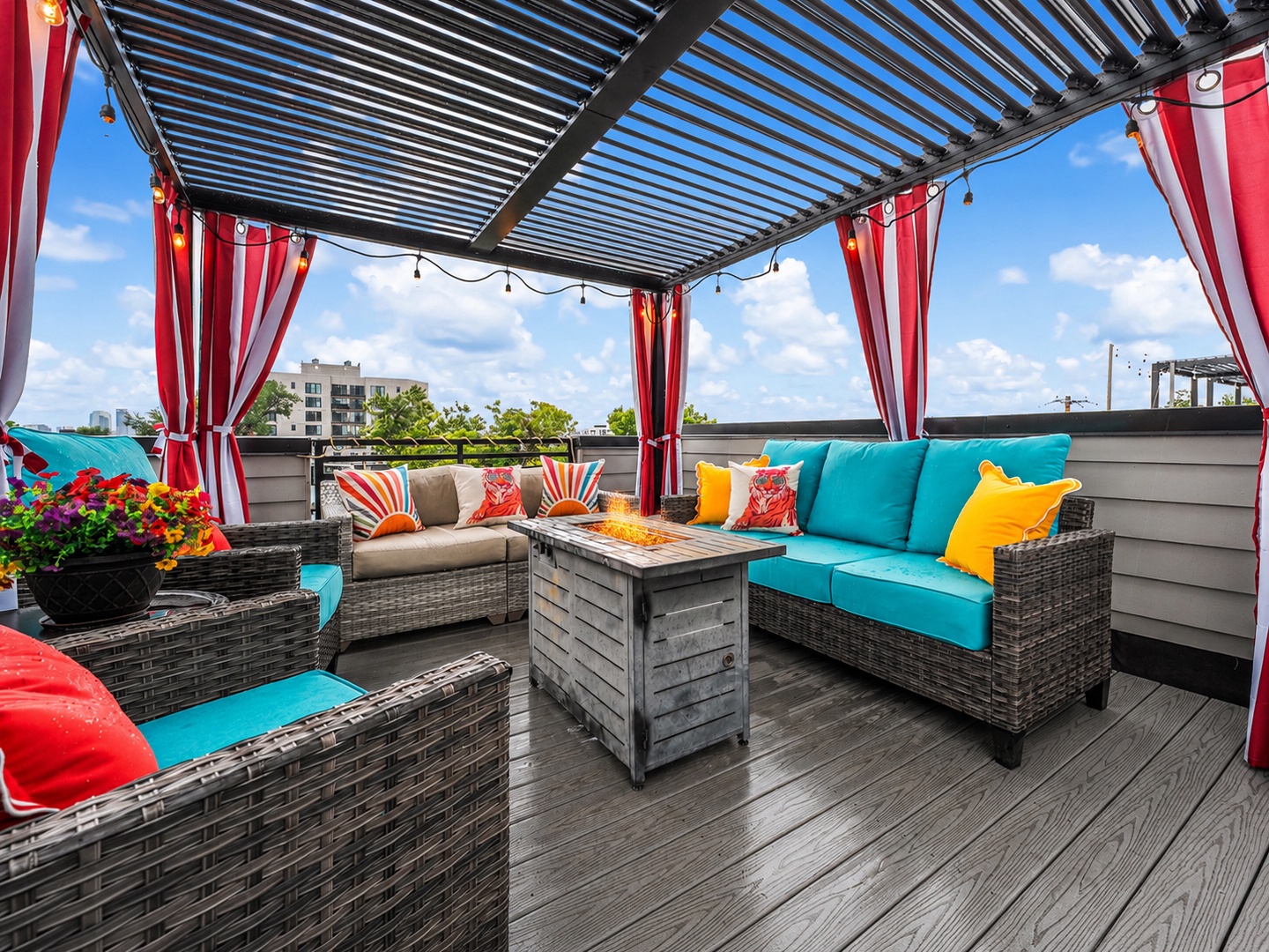 Bright turquoise cushions and bold pops of color invite you to unwind on this stylish rooftop terrace, where string lights and breezy curtains create your perfect outdoor escape.