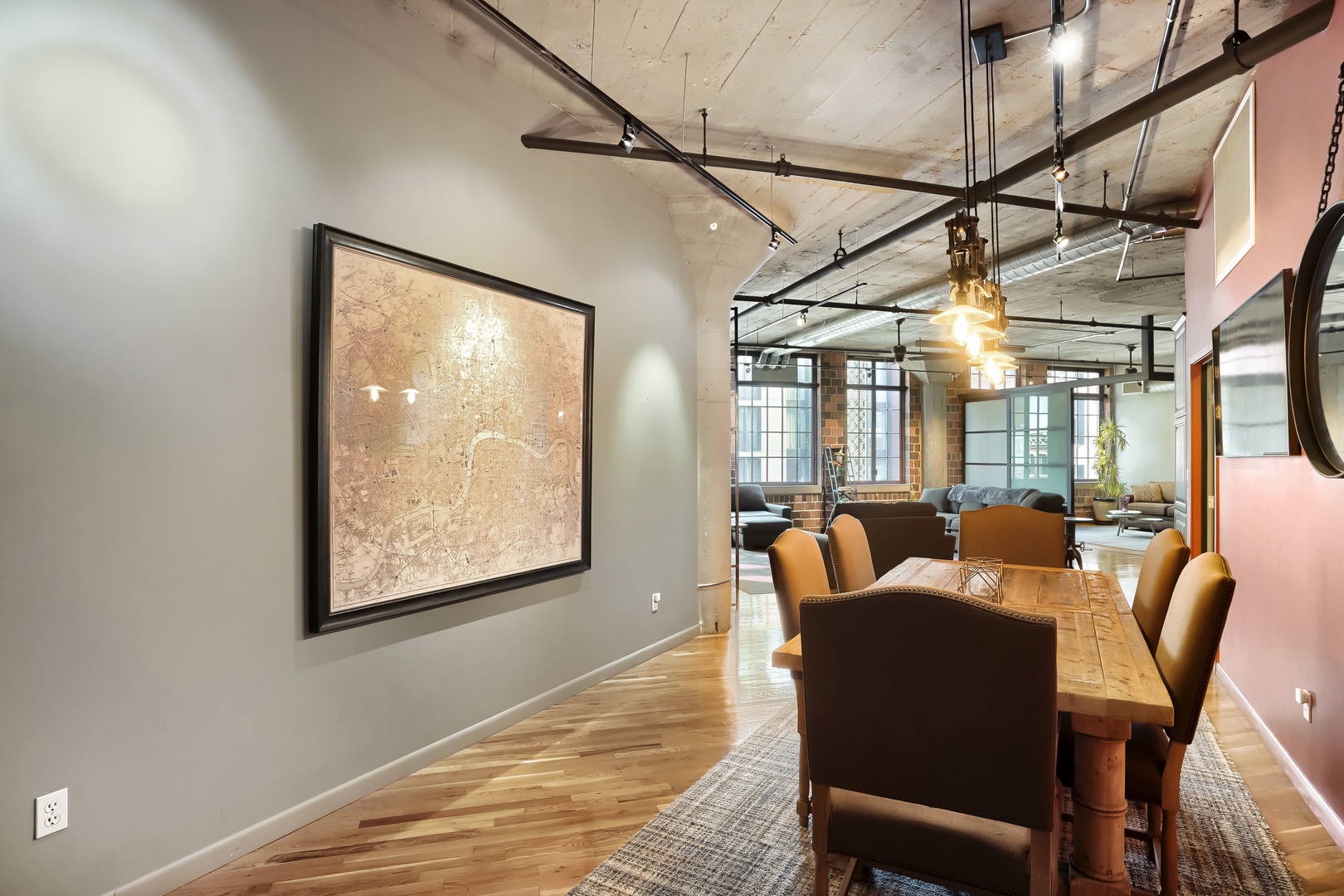 Gather around the rustic dining table under industrial pendant lights, where warm wood floors and modern accents create an inviting space for your meals and conversations.