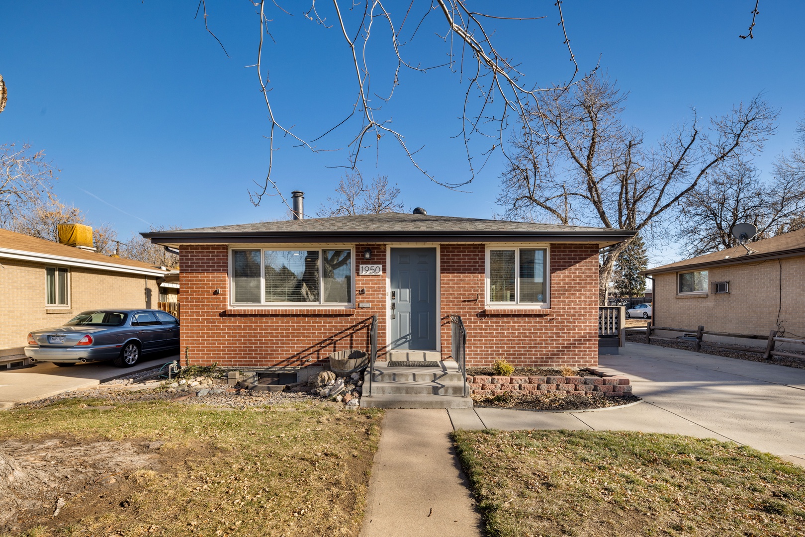 Charming brick ranch home with spacious driveway and peaceful residential setting under clear blue skies.