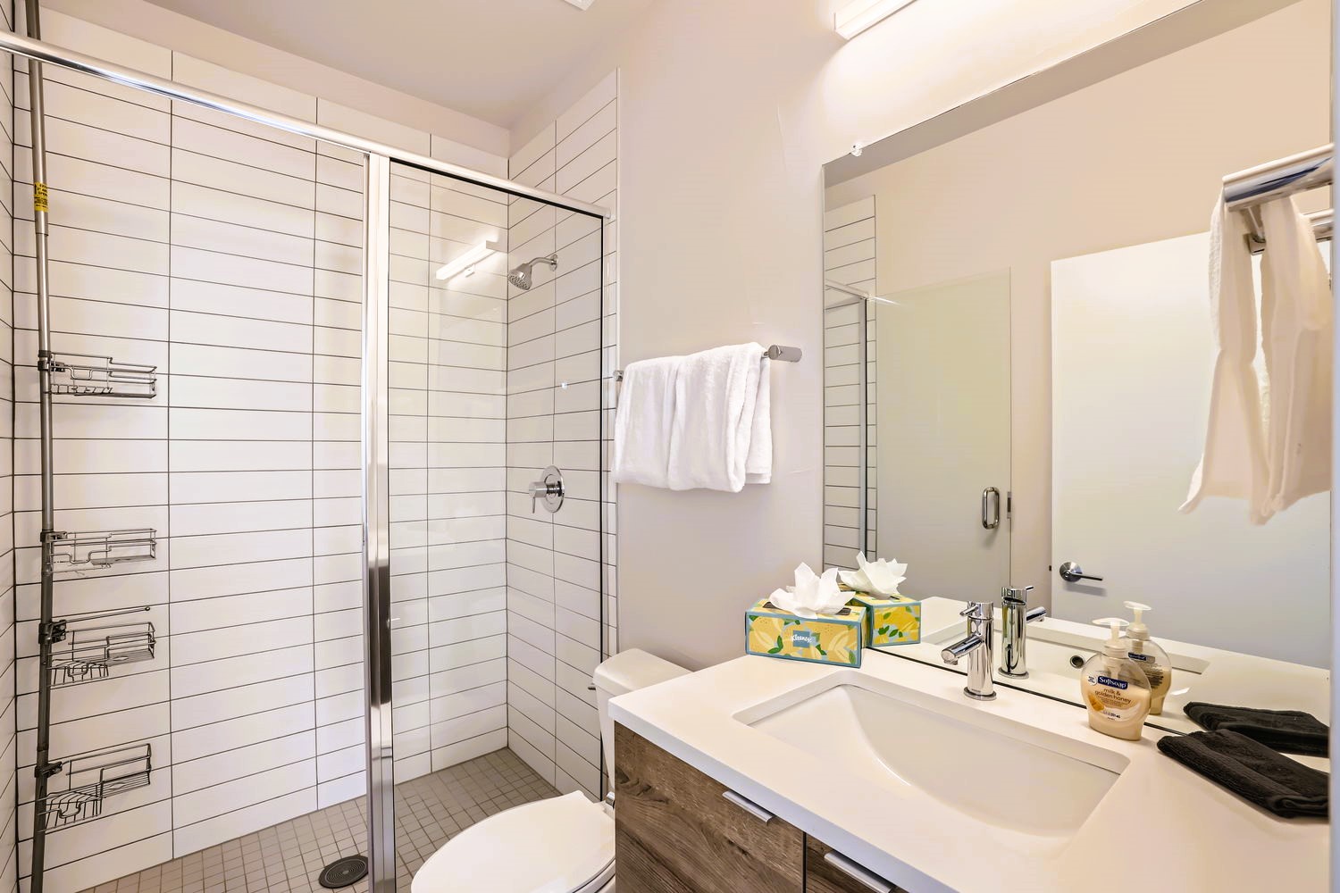 Your private bathroom features a sleek glass shower, crisp white tiles, and thoughtful touches like fresh towels and toiletries waiting for your arrival.