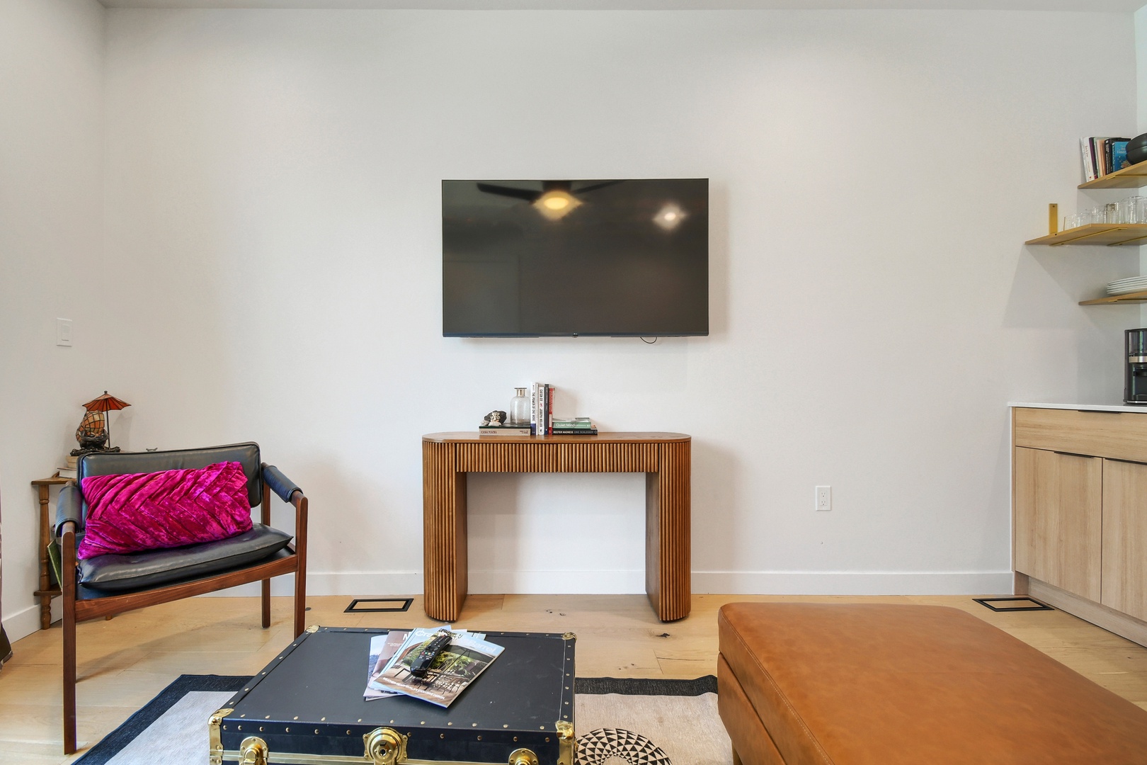 Unwind in your bright, minimalist living space featuring a sleek entertainment setup and comfortable seating. The open layout and warm wood accents create a relaxing retreat for your stay.