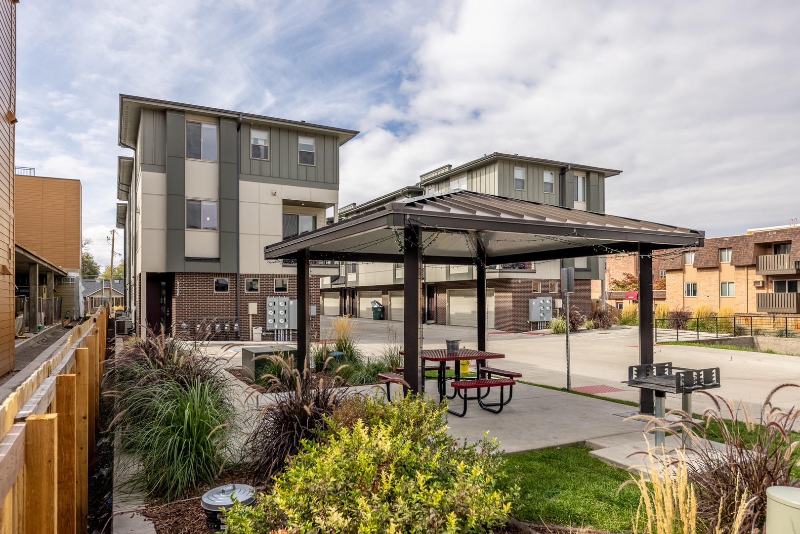 A quiet neighborhood with modern multi-story residences and a shared courtyard featuring covered seating and green landscaping