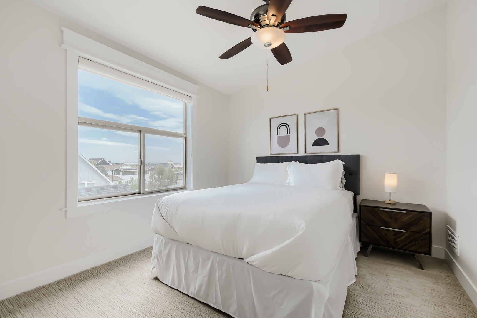 Sink into crisp white linens and wake to peaceful neighborhood views. Your ceiling fan and modern art create a serene retreat for restful nights.