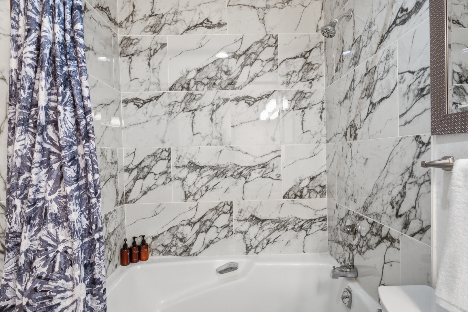 Luxurious marble-tiled bathroom with a sleek tub-shower combo, where you can unwind under elegant finishes and modern fixtures after a day of exploring.