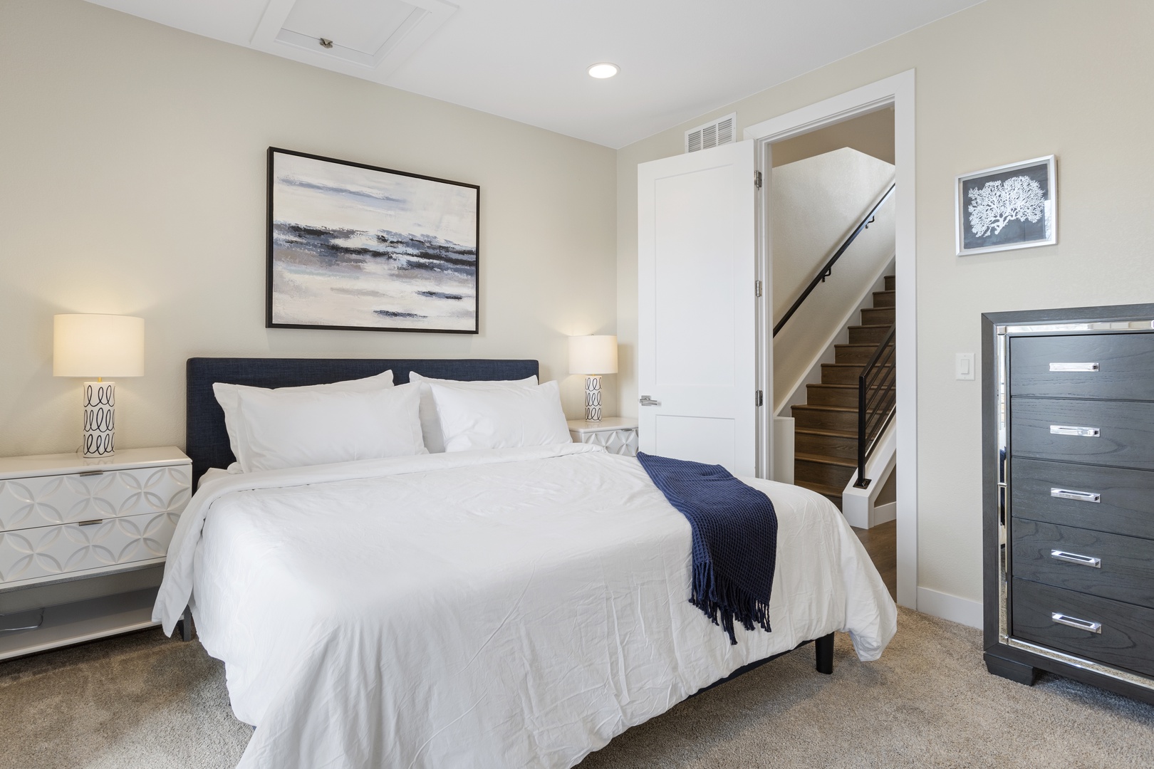 Sink into crisp white linens and peaceful blue accents in your elegantly appointed bedroom, complete with stylish furnishings and serene coastal artwork.