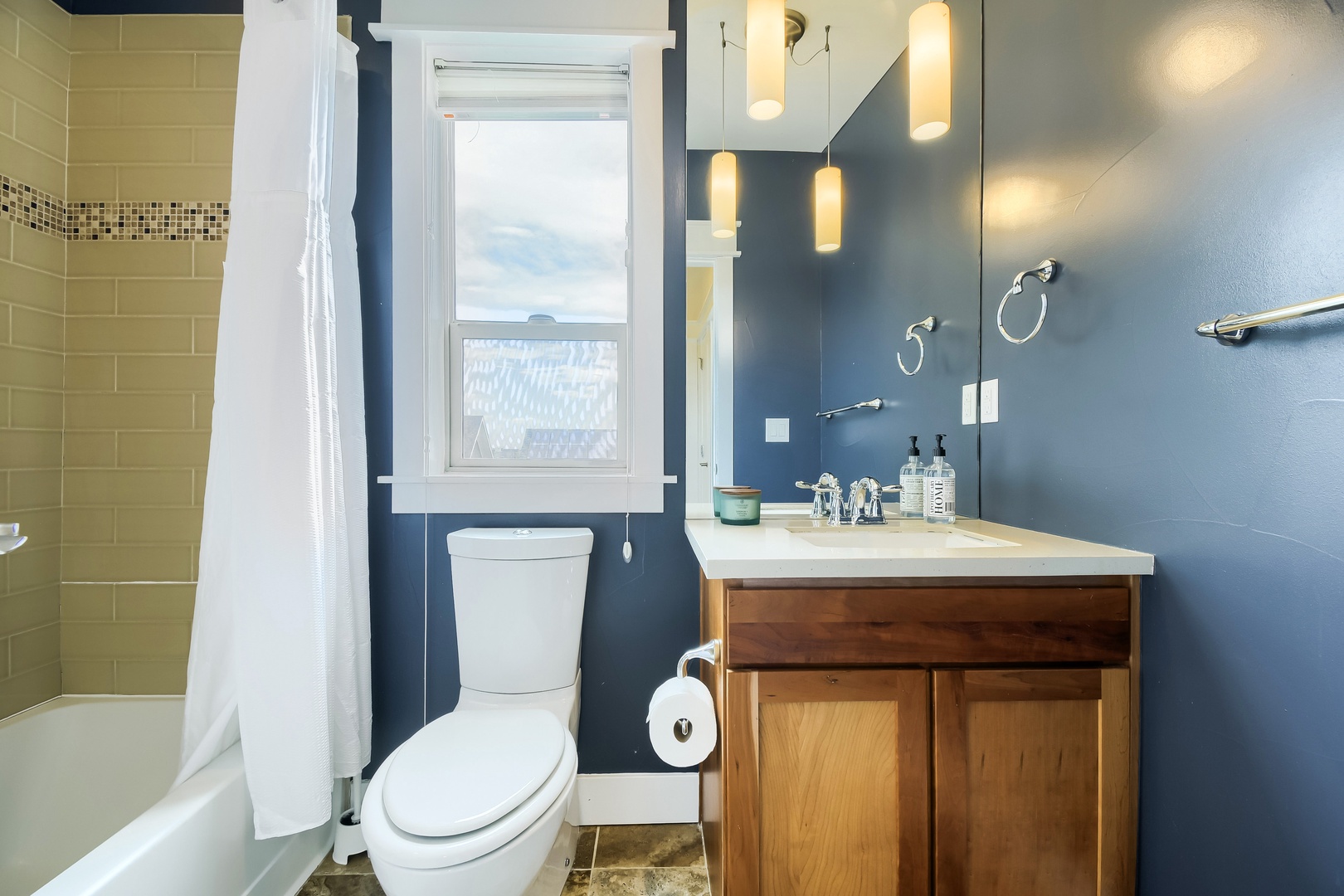 Step into your stylish bathroom featuring modern blue walls, warm wood vanity, elegant lighting, and a refreshing shower-tub combo—your personal retreat after a day of adventure.