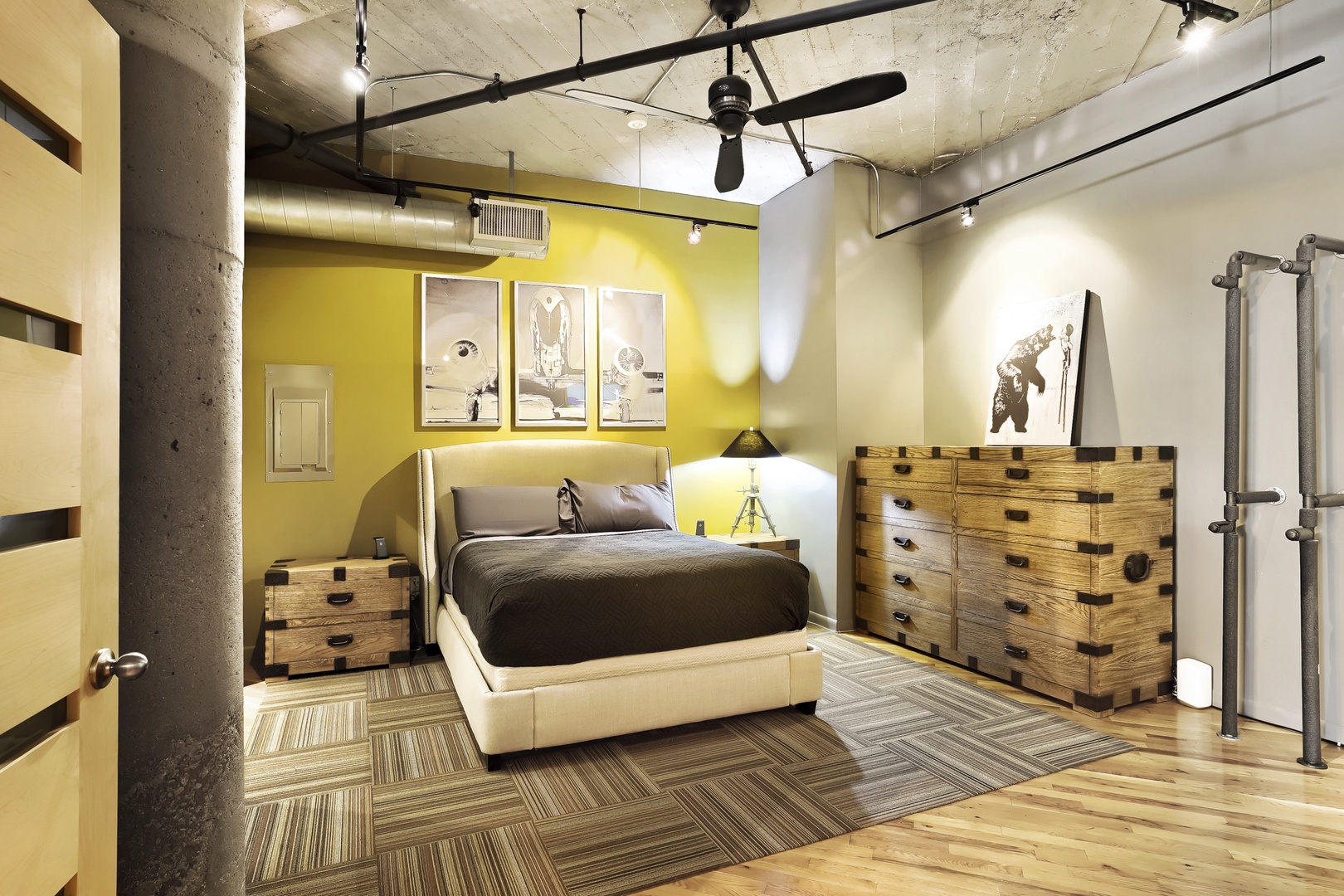 Sink into the plush bed and let the bold yellow accent wall energize your stay in this uniquely styled loft bedroom with exposed concrete and warm wooden furnishings.