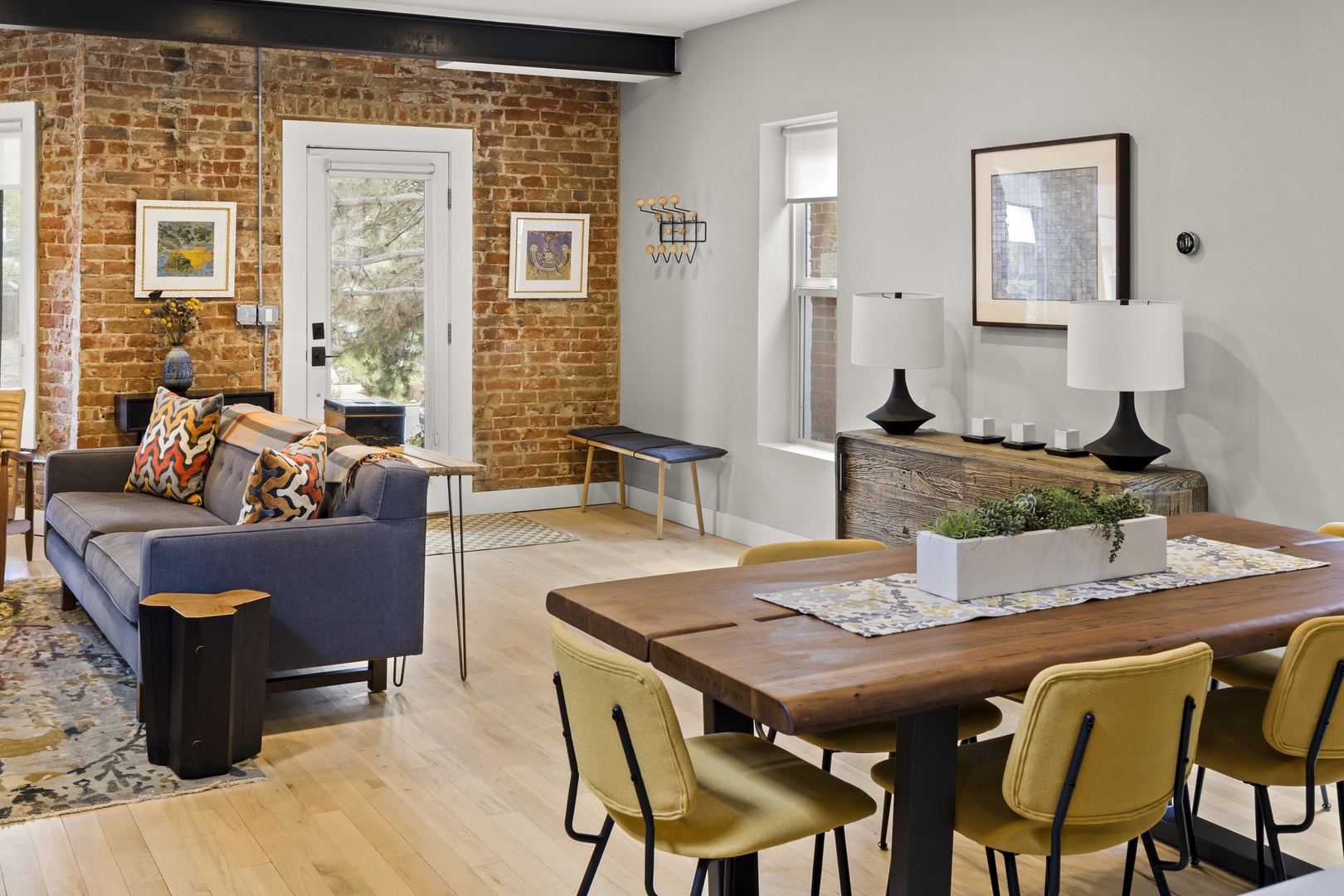 You'll love this stylish open-plan living space where exposed brick walls meet modern comfort, perfect for relaxing on the sofa or gathering around the wooden dining table.