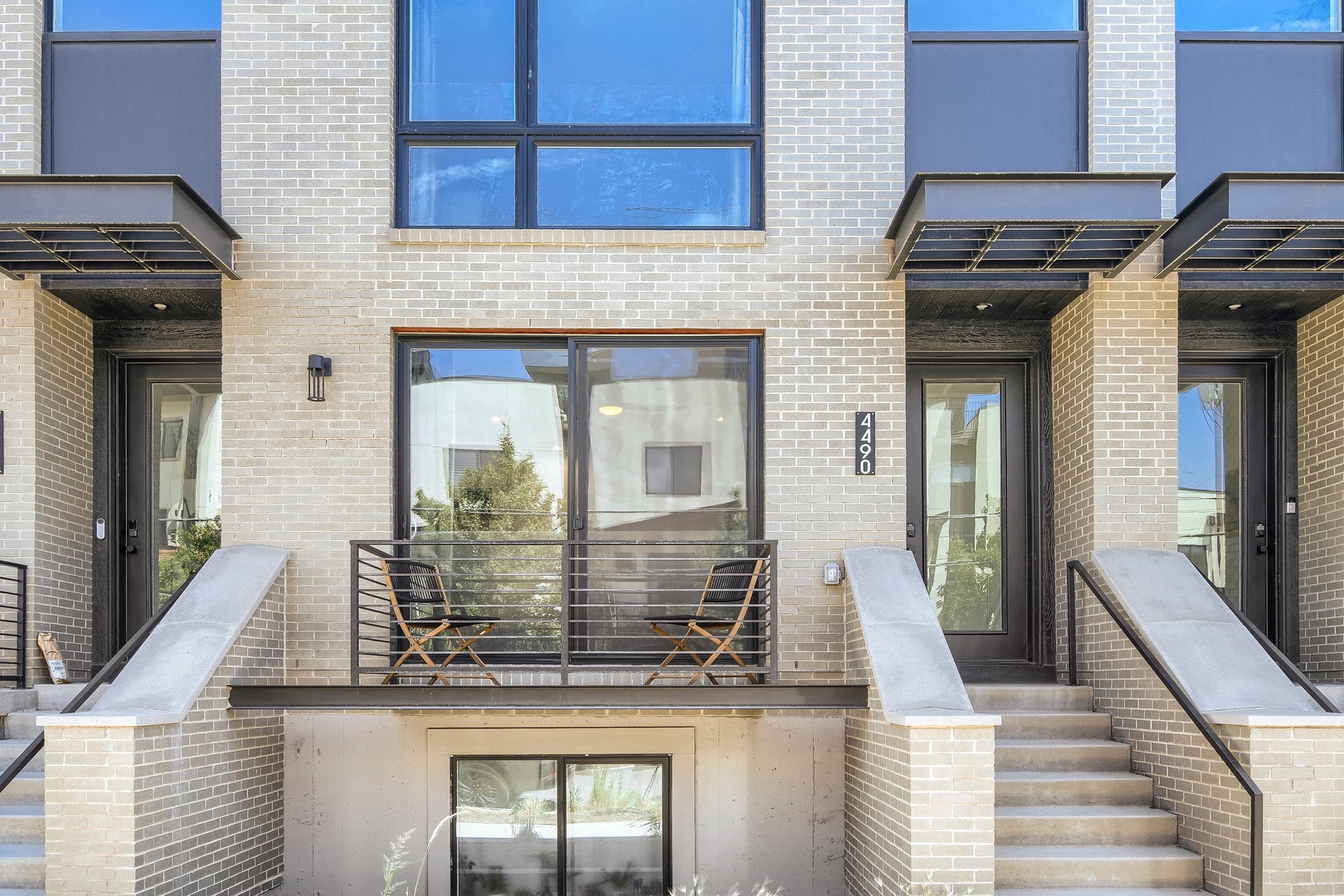 Modern urban residential building with clean lines, white brick facade, and private entrances. Contemporary architecture blends style with functionality in a well-maintained neighborhood.