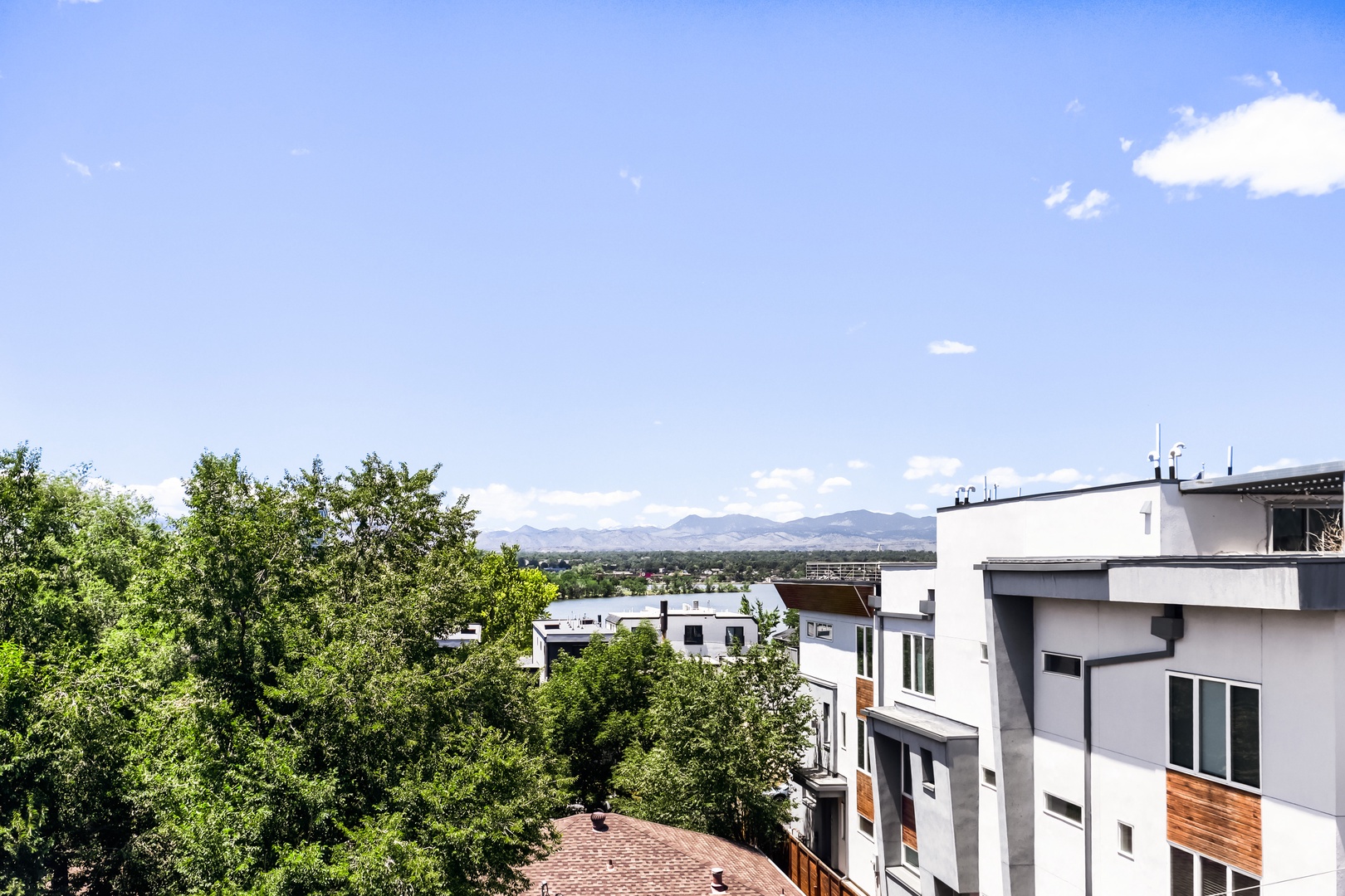 Modern multi-story buildings nestled among lush trees with distant mountain ranges under a clear blue sky, defining the neighborhood's scenic setting.