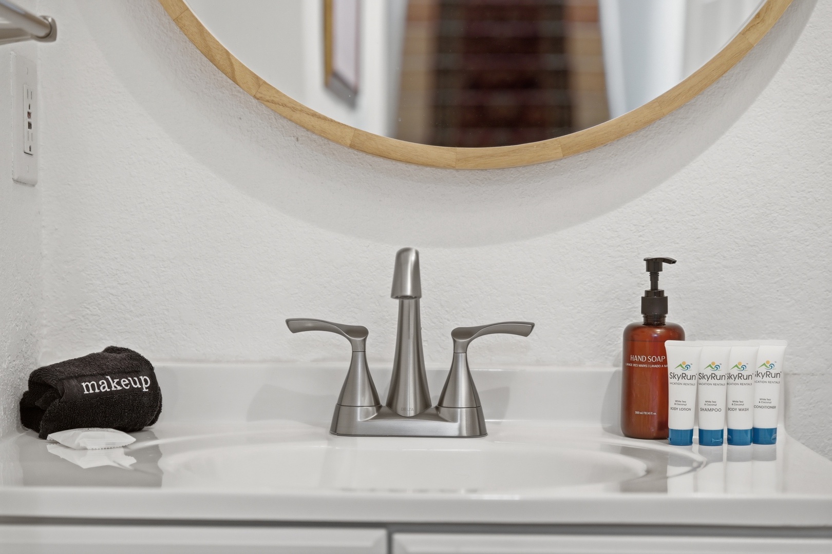 Your modern bathroom vanity features a sleek sink, stylish round mirror, and thoughtfully placed amenities—fresh towels, hand soap, and travel-sized toiletries ready for your arrival.