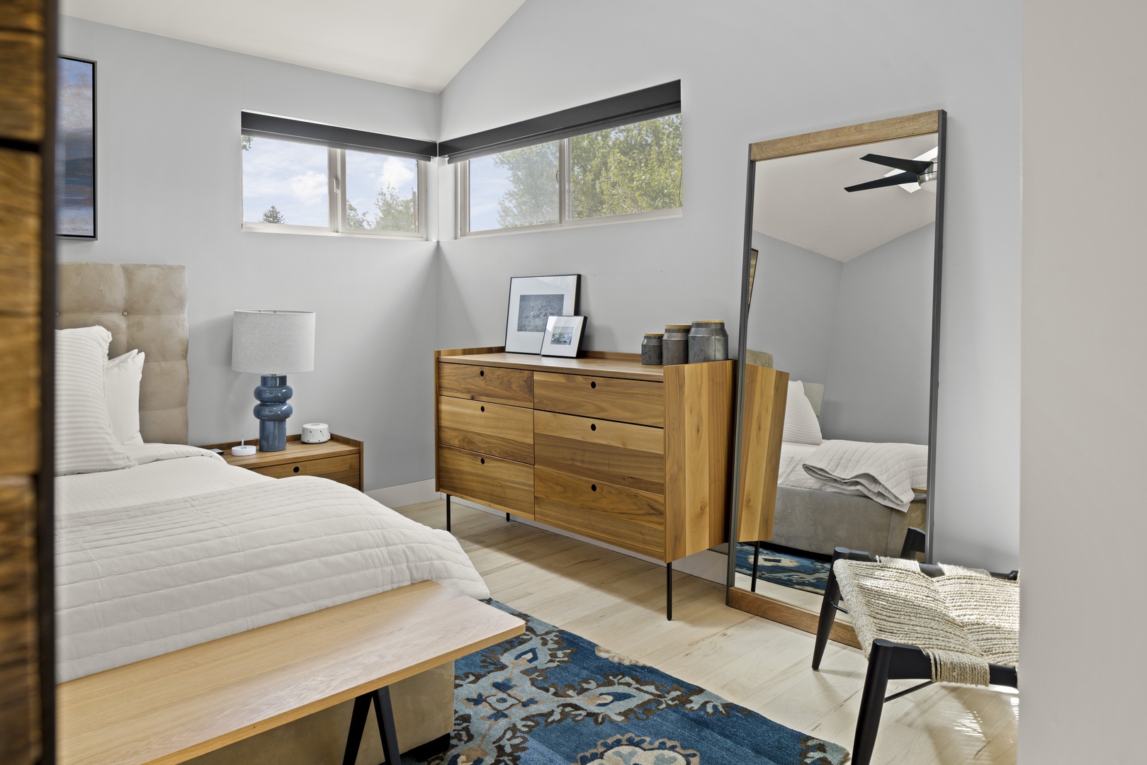 Unwind in your serene bedroom with modern touches, warm wood furniture, and natural light streaming through corner windows.