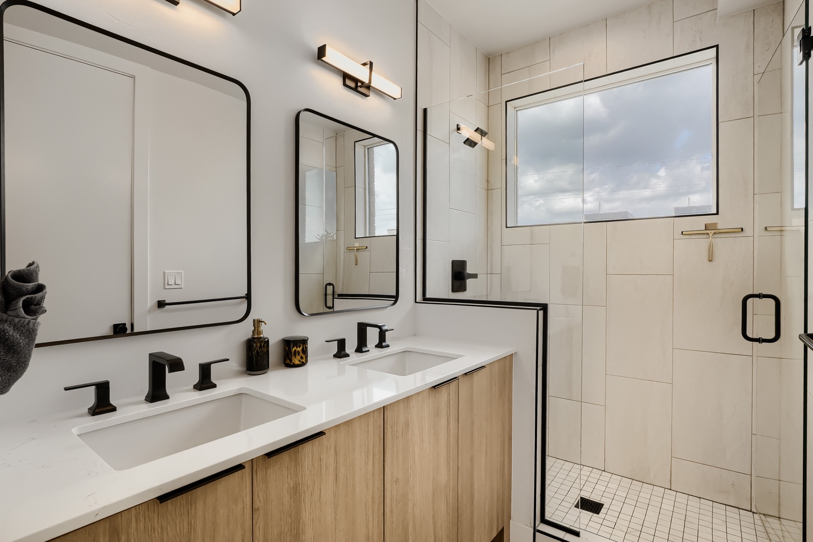 Refresh in your bright modern bathroom with dual vanities and a spacious walk-in shower featuring sleek black fixtures and natural light streaming in.