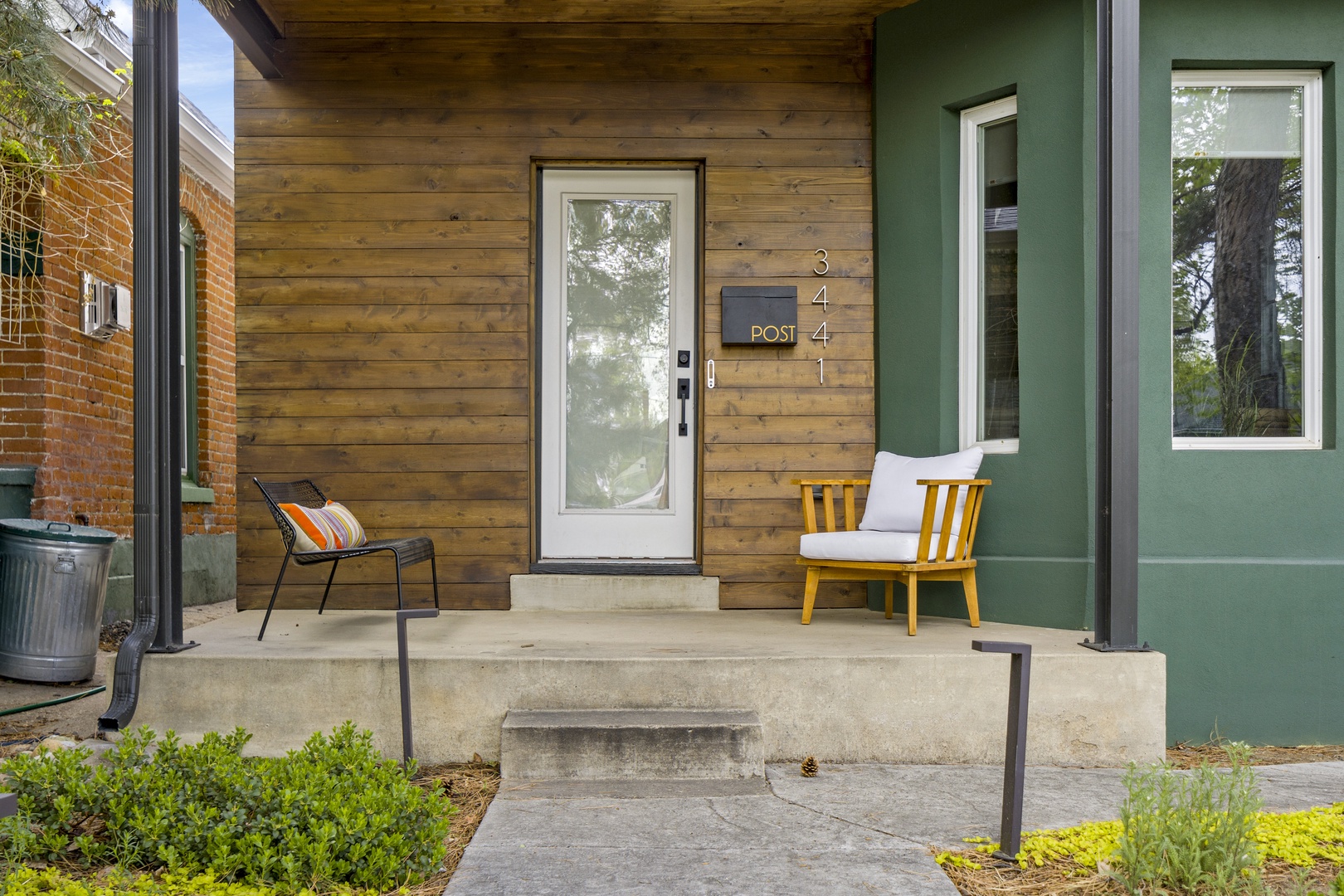 Modern property entrance featuring green siding, natural wood accents, and welcoming front porch seating area.