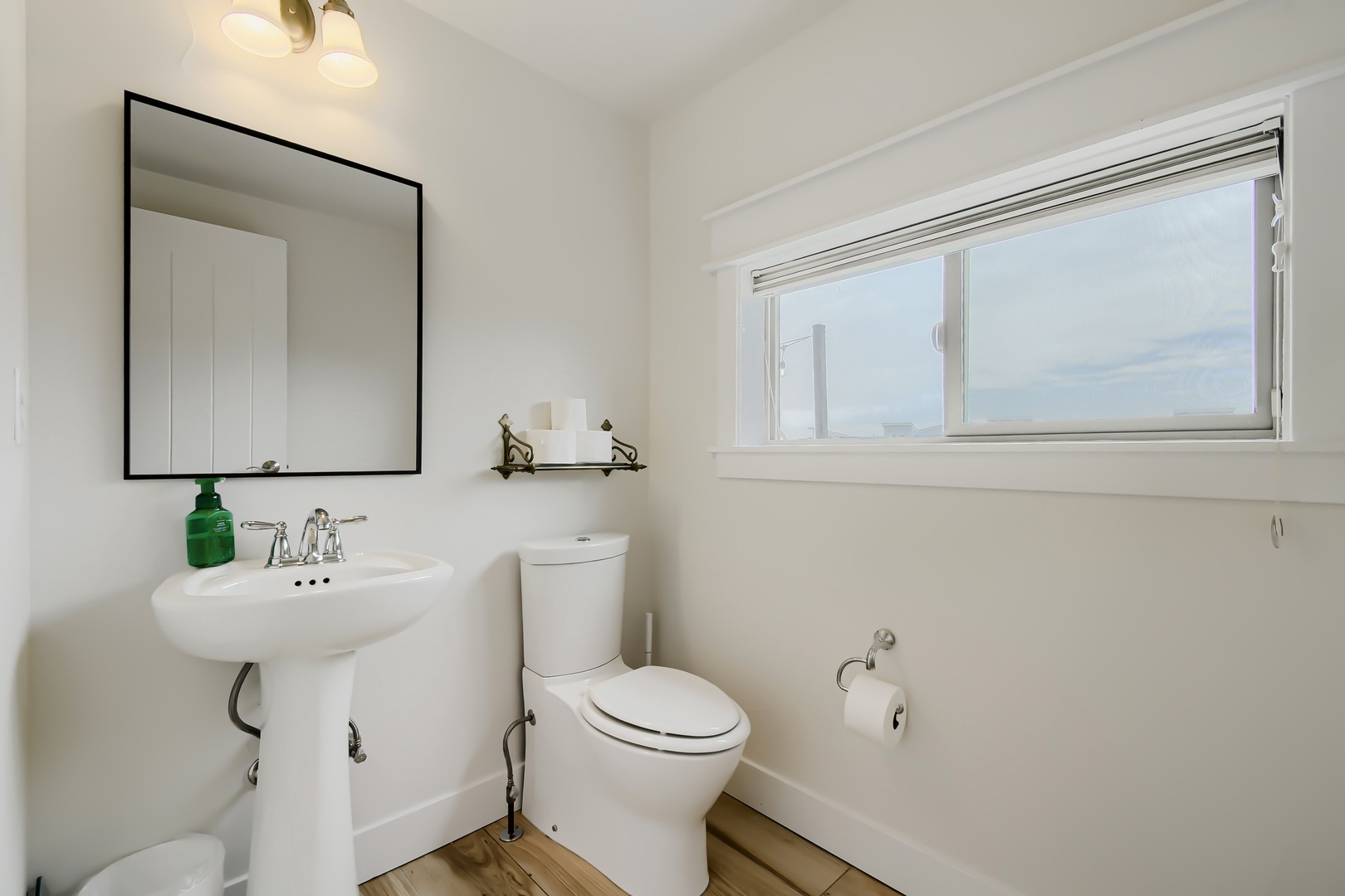Your private bathroom features a classic pedestal sink, modern toilet, and natural light streaming through the window, creating a fresh and welcoming space for your stay.
