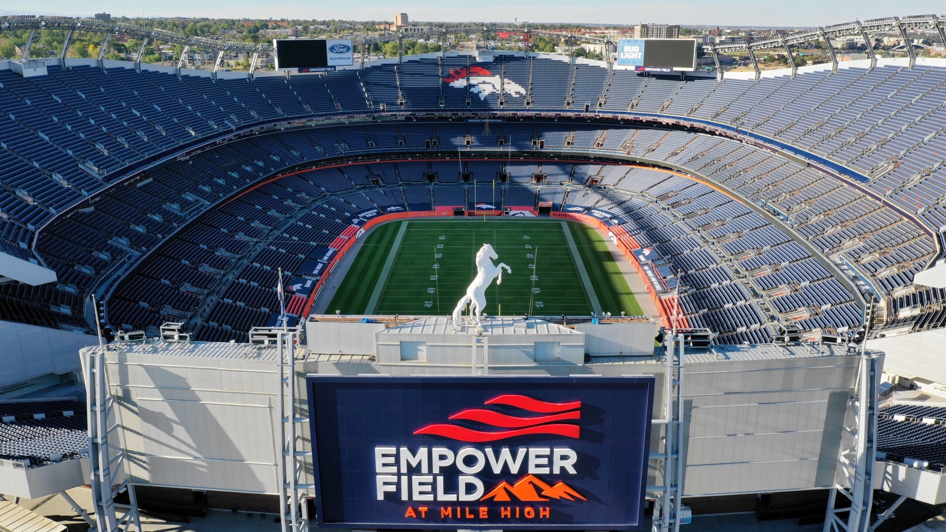 Aerial view of Denver's iconic Empower Field at Mile High Stadium, featuring the famous Broncos horse statue and downtown Denver skyline.