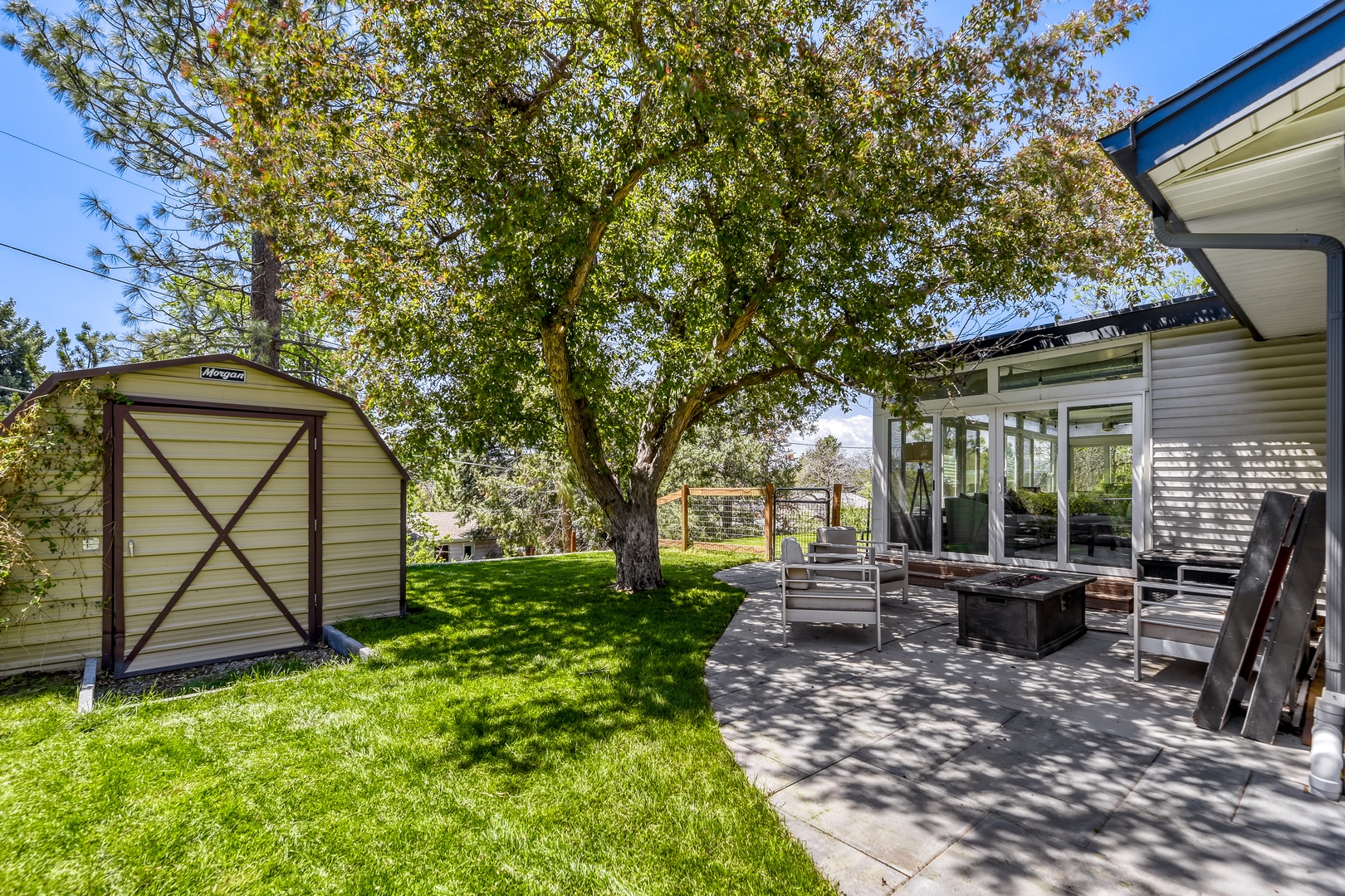 Modern vacation home nestled in a tranquil setting with a shaded patio, lush lawn, and mature tree—perfect for outdoor relaxation and sunny day retreats.
