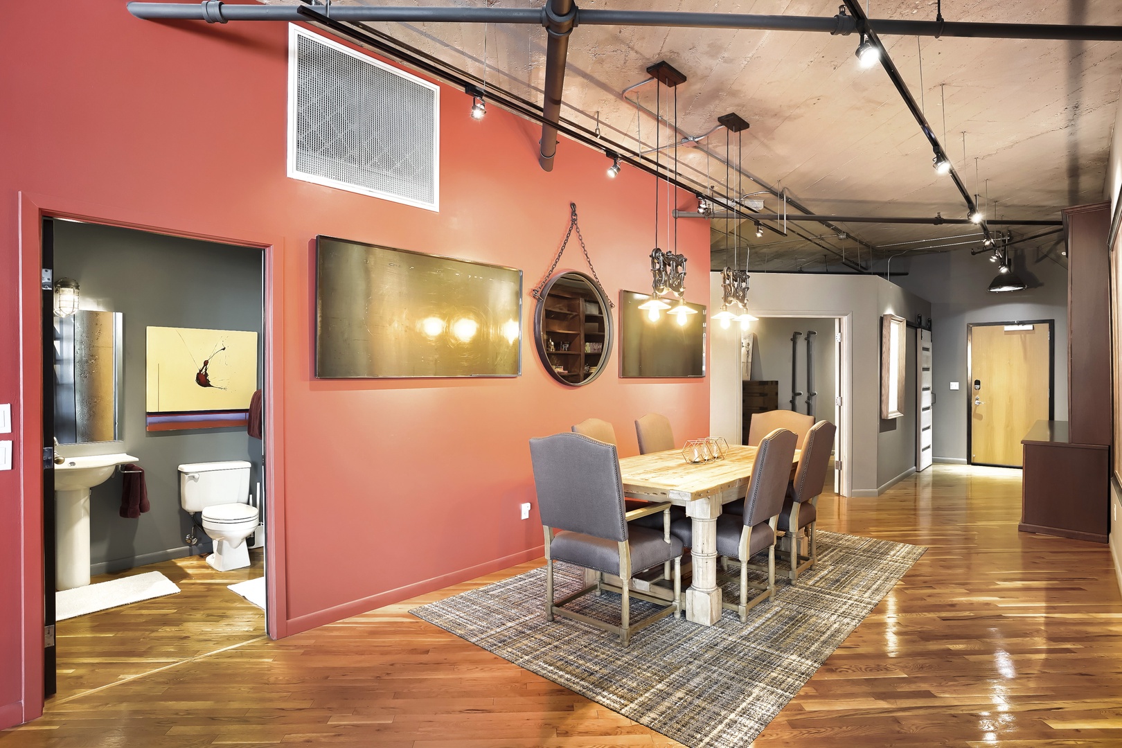 Your open-concept dining area features warm coral walls, exposed ceilings, and gleaming hardwood floors. Gather around the farmhouse table under pendant lights for memorable meals with loved ones.