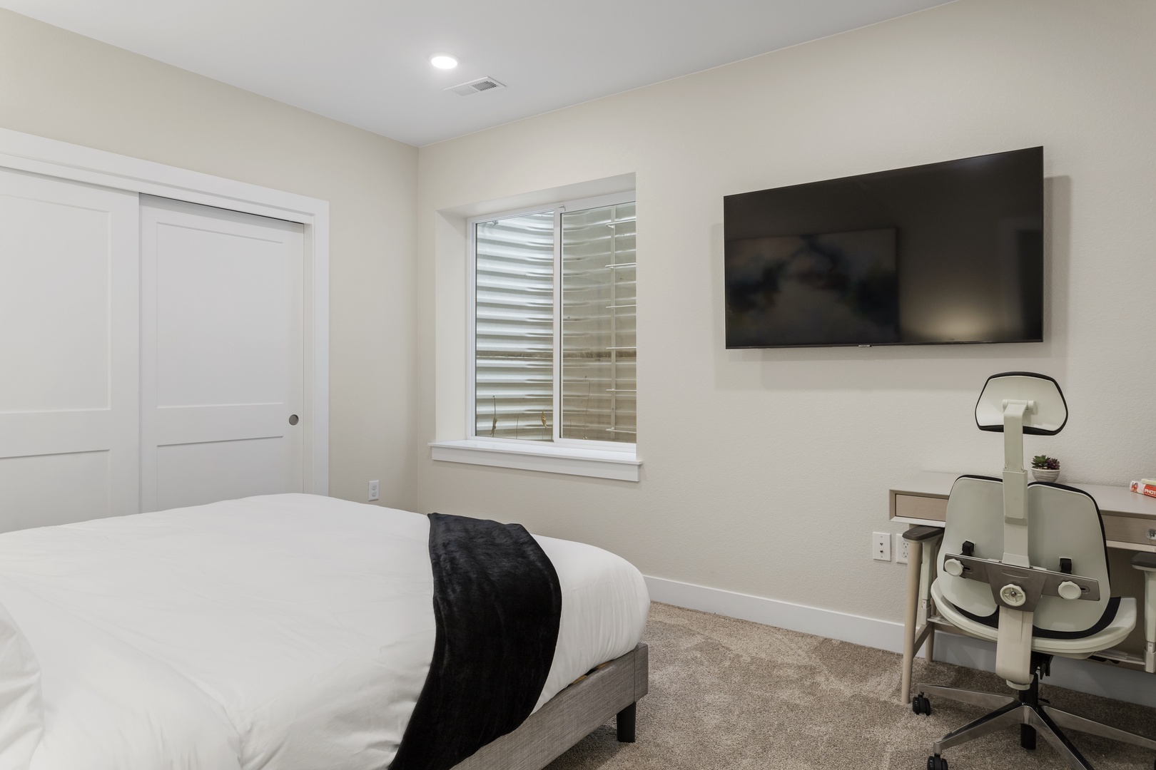 Rest peacefully in your modern bedroom with plush bedding, wall-mounted TV, and dedicated workspace for productivity.