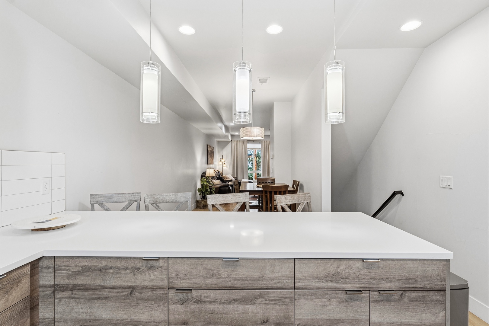 This modern kitchen features sleek white quartz countertops, warm wood cabinetry, and pendant lighting that creates a welcoming space for preparing meals and gathering with loved ones.