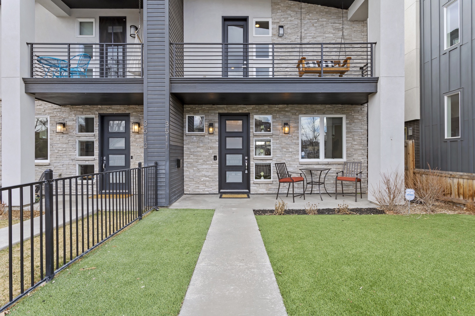 Modern townhouse featuring stone and siding exterior with private patio seating and upper balcony in contemporary neighborhood setting.