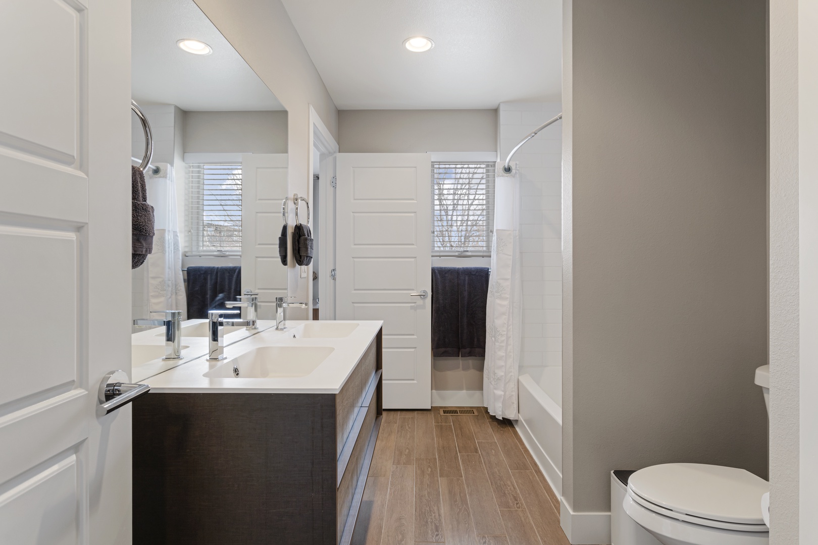 Step into your spacious bathroom with modern fixtures, warm wood floors, and bright natural light streaming through the windows.