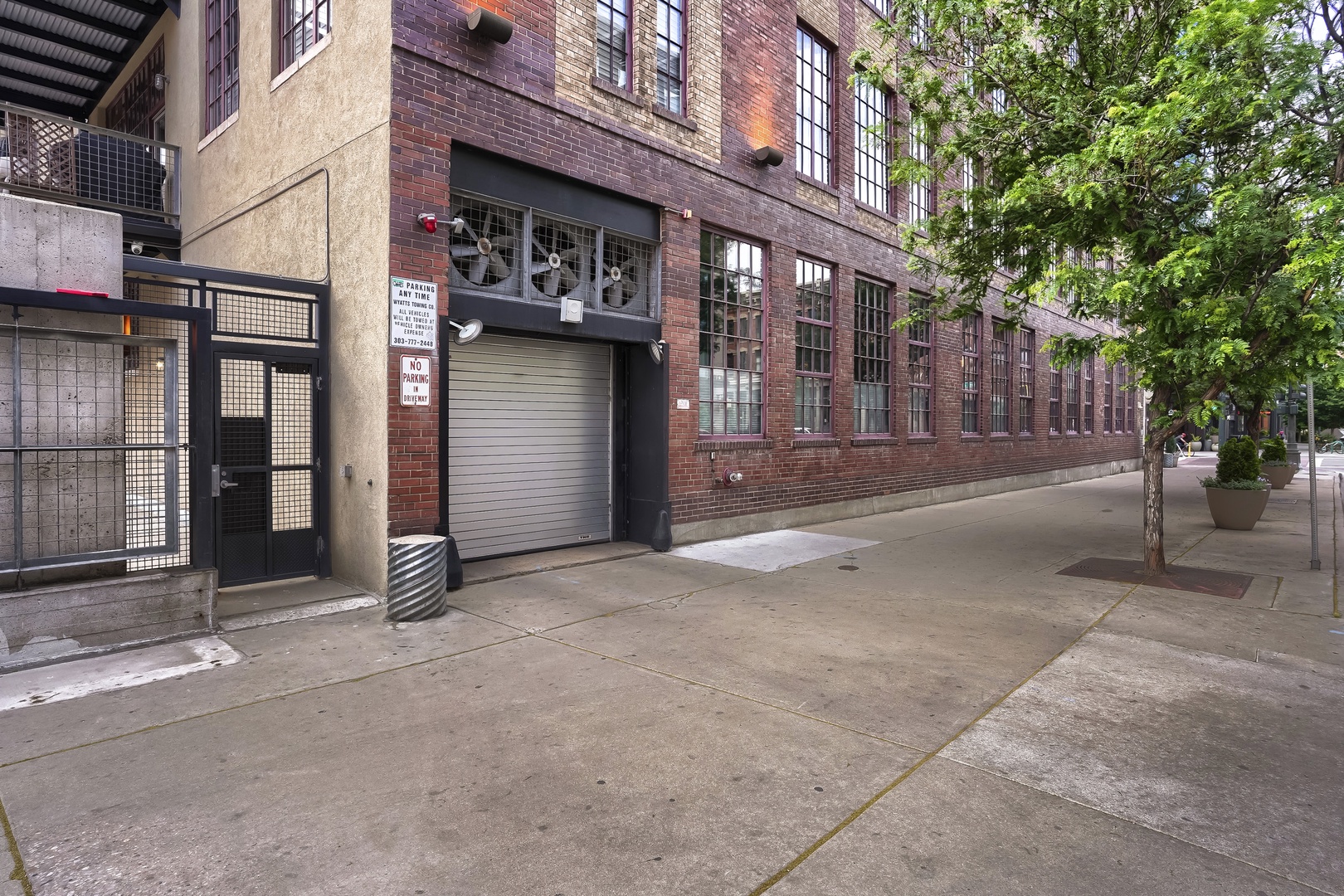 A converted industrial brick building with large multi-pane windows on a tree-lined street, offering a unique urban character and setting.