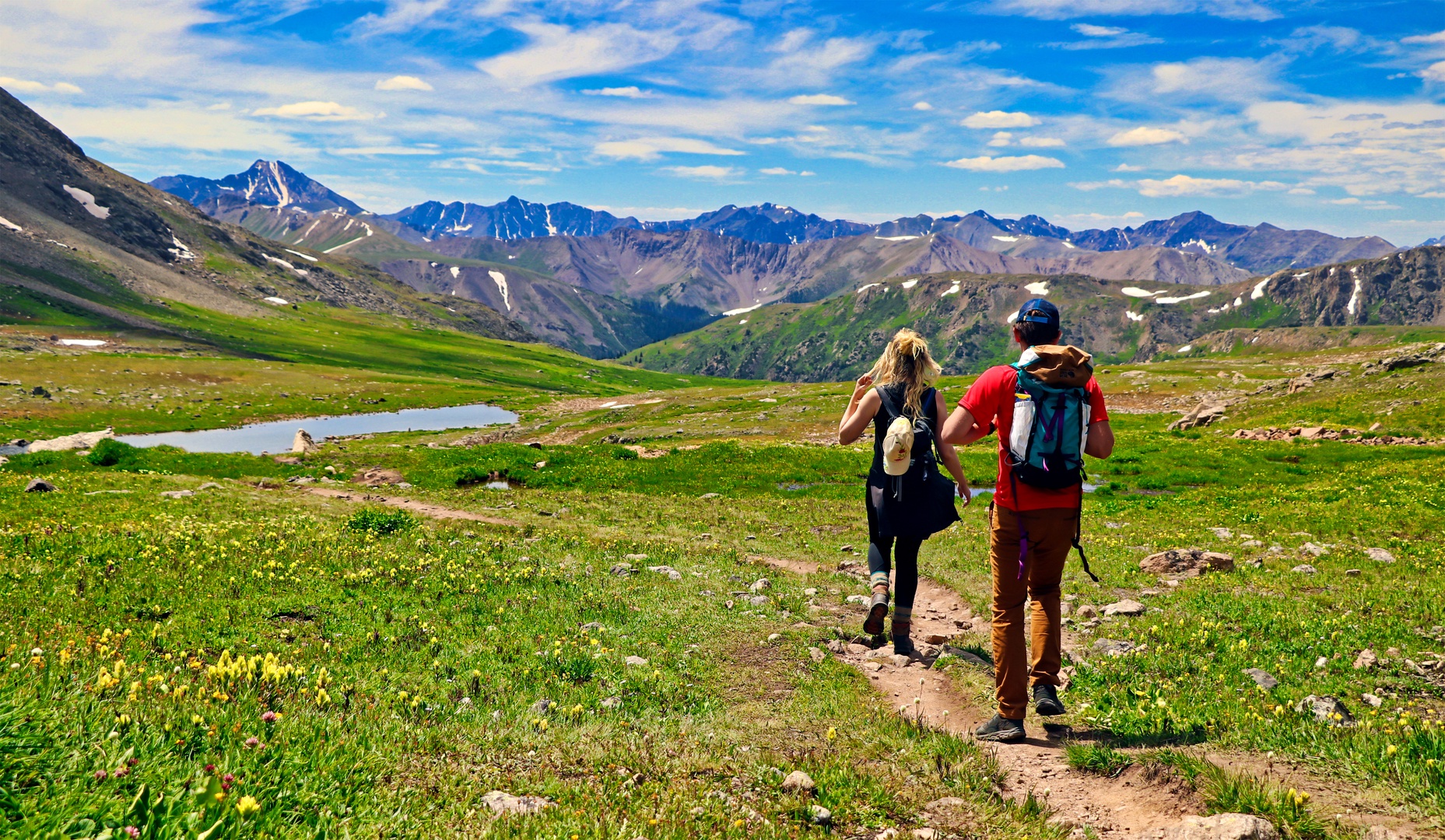A scenic hiking trail winds through alpine meadows with dramatic mountain ranges in the distance, showcasing the stunning natural landscape surrounding the property.