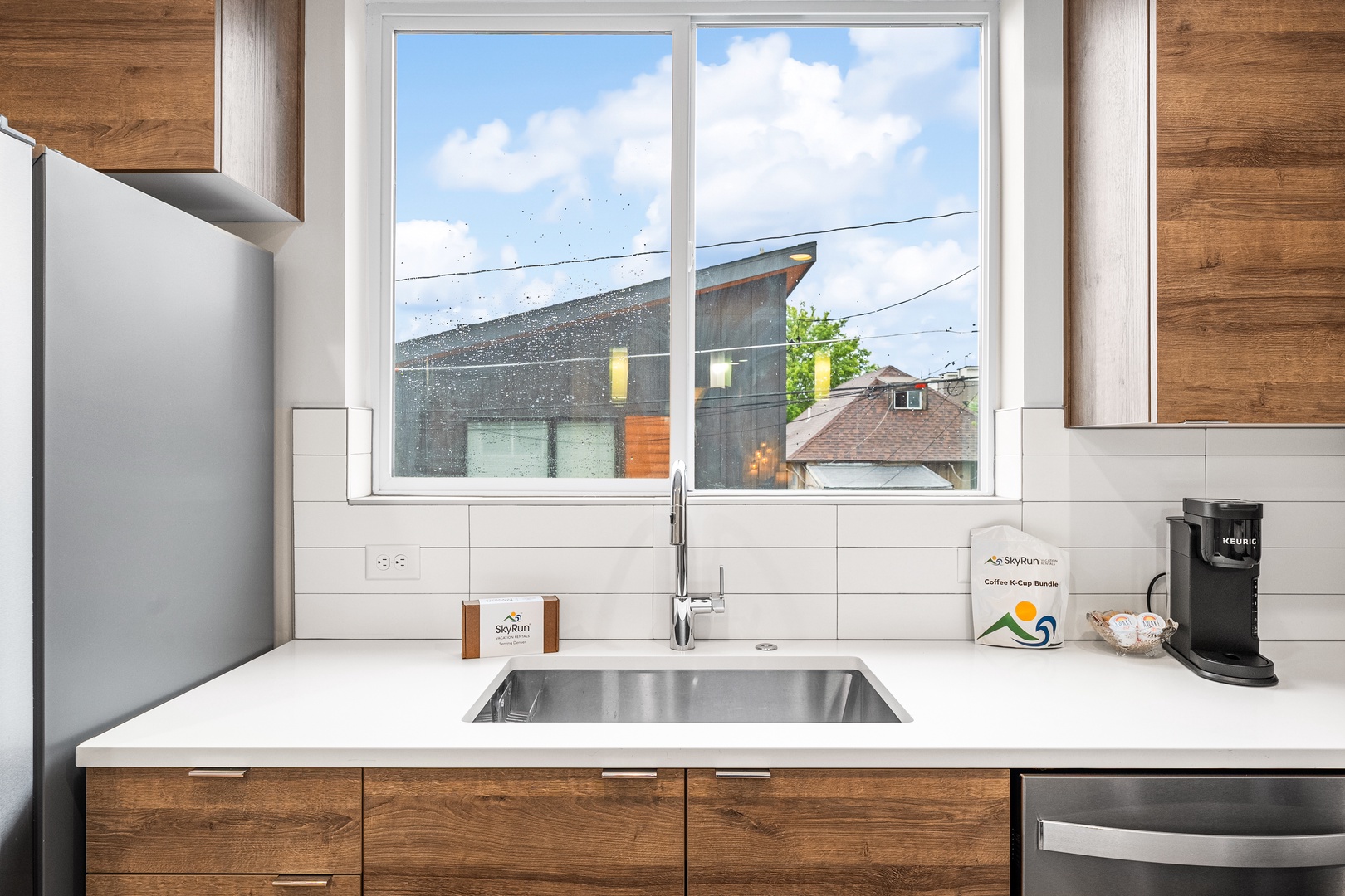 Your modern kitchen features sleek countertops, warm wood cabinetry, and a coffee station ready for leisurely mornings. Natural light floods the space through large windows overlooking the neighborhood.