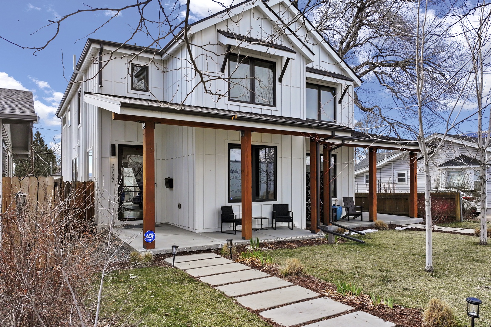 Modern two-story home featuring white board-and-batten siding with warm wood accents and a welcoming covered porch in a quiet residential neighborhood.
