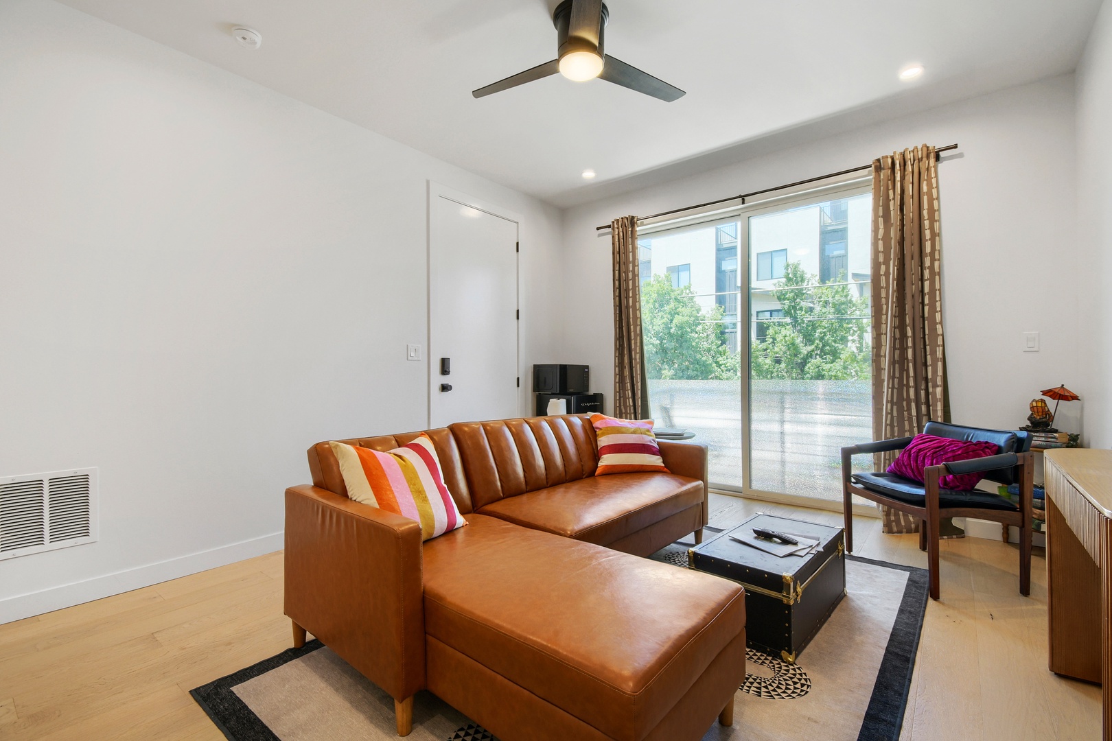 Settle into your stylish living room, where a plush leather sectional invites you to unwind beneath the gentle breeze of the ceiling fan. Natural light pours through expansive windows, framing your private outdoor terrace.