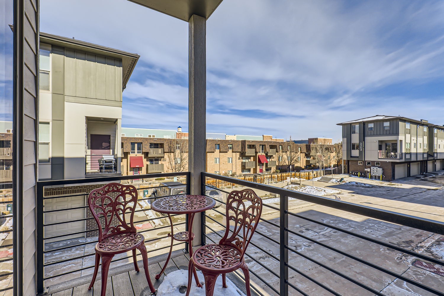 A covered balcony with cozy seating overlooks a modern residential neighborhood, offering fresh air and peaceful neighborhood views in a convenient urban setting.