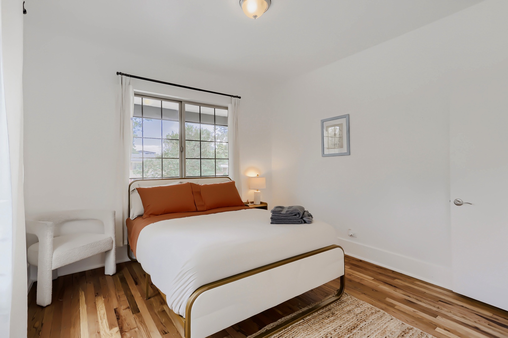 Your serene bedroom offers a comfortable bed with crisp linens, warm wood floors, and natural light streaming through the window—your peaceful retreat after a day of exploring.