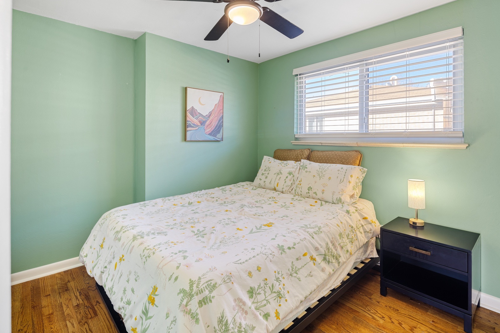 Drift off to sleep in this tranquil bedroom with soothing green walls, botanical bedding, and gentle ceiling fan breeze.