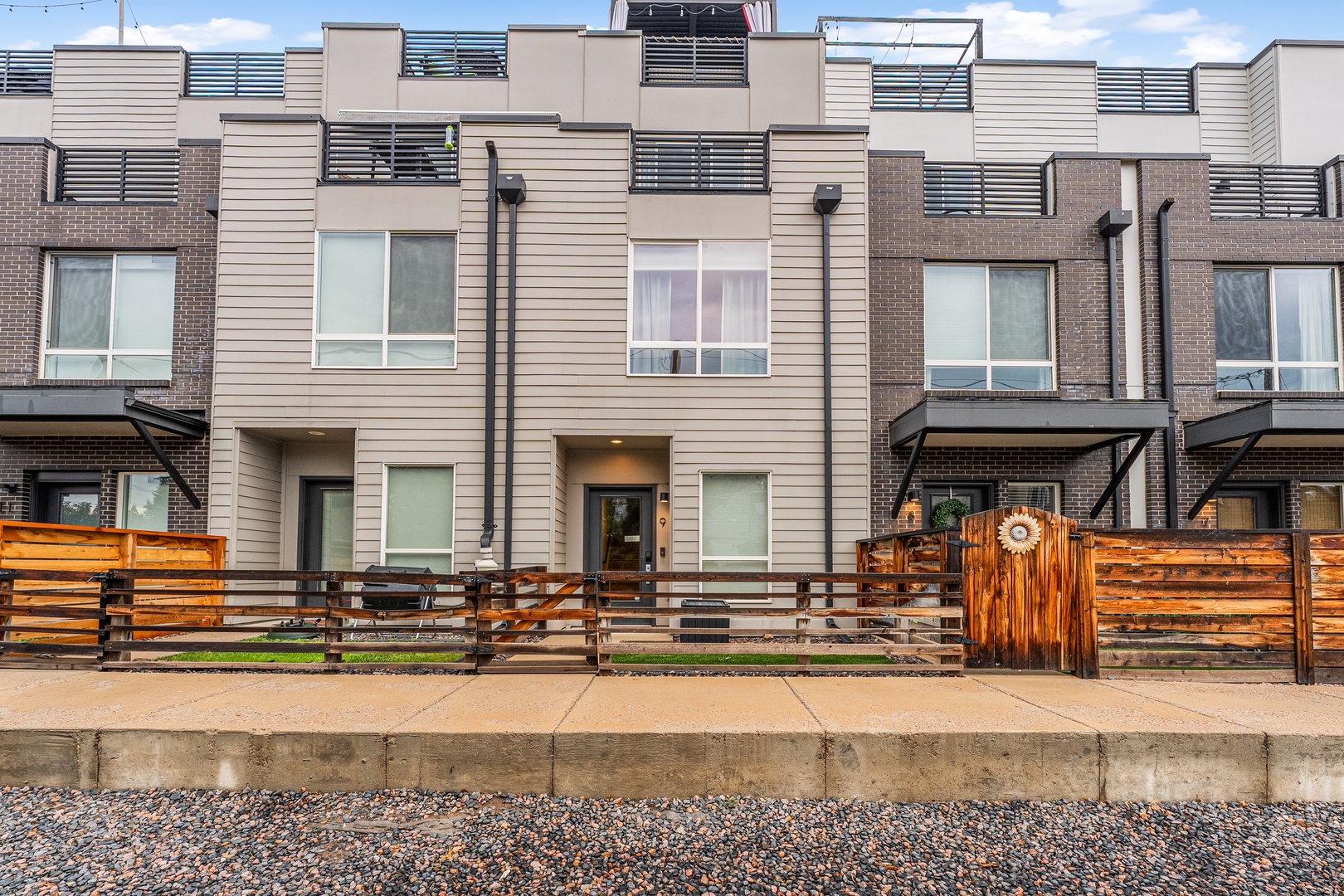 Modern townhome exterior with inviting wooden-fenced patio areas, offering a stylish residential retreat in a well-designed neighborhood setting.