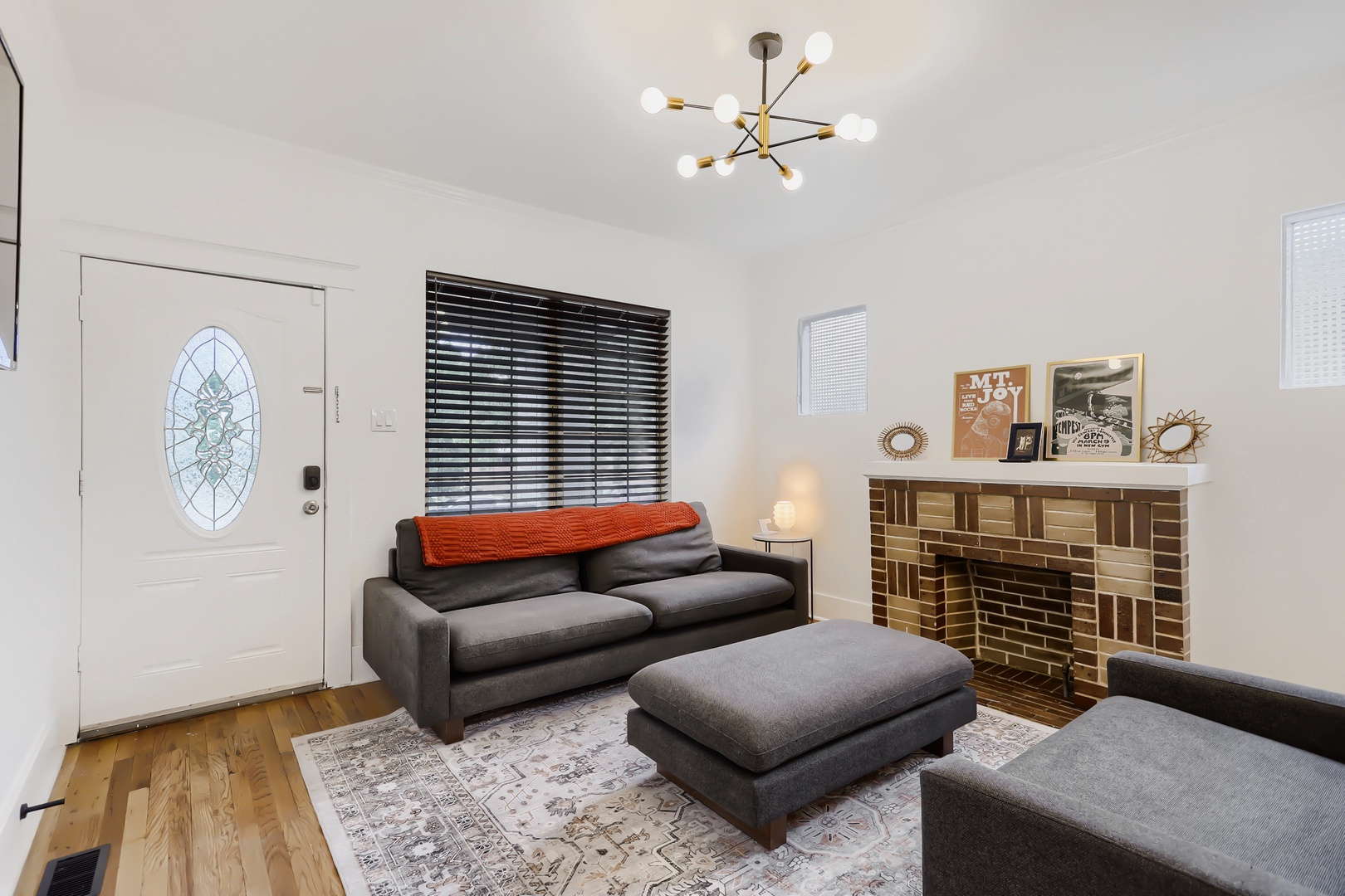 Your cozy living room features mid-century charm with a modern sofa, stylish light fixture, and unique decorative fireplace—perfect for unwinding after exploring the neighborhood.