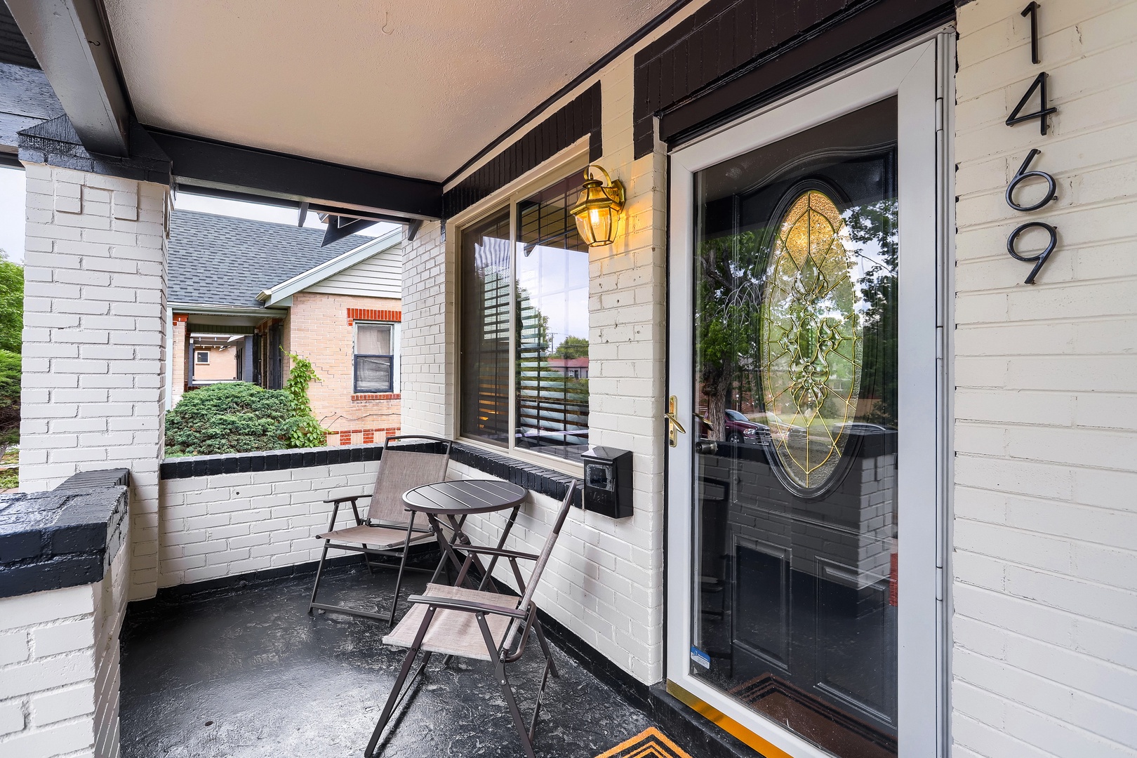 A charming entry porch with bistro seating creates an inviting arrival experience at this property, marked by distinctive address numbers and warm outdoor lighting.