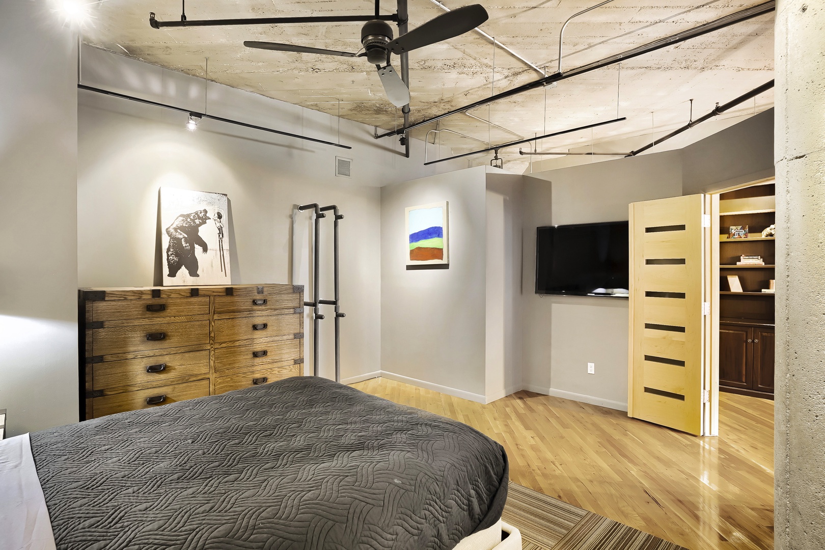 Relax in your stylish urban retreat with sleek concrete ceilings, exposed industrial design, original artwork, and a ceiling fan for your comfort. The space flows seamlessly into additional rooms.