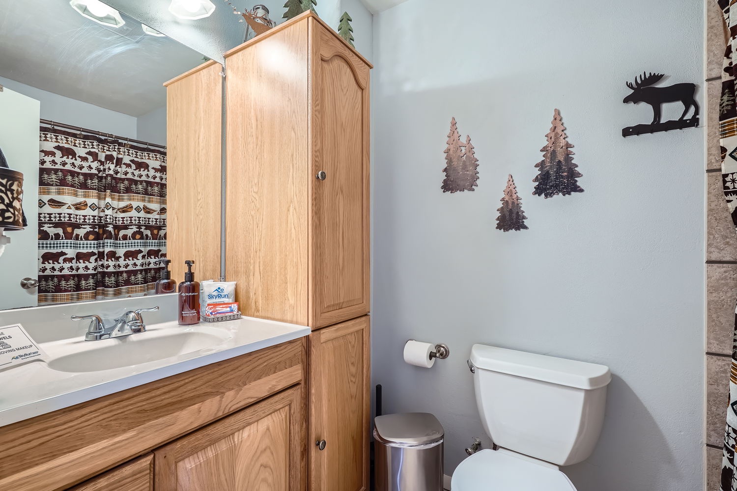 Step into a charming bathroom with rustic woodland décor. The cabinet offers plenty of storage, while playful moose and tree accents create a cozy mountain retreat atmosphere.