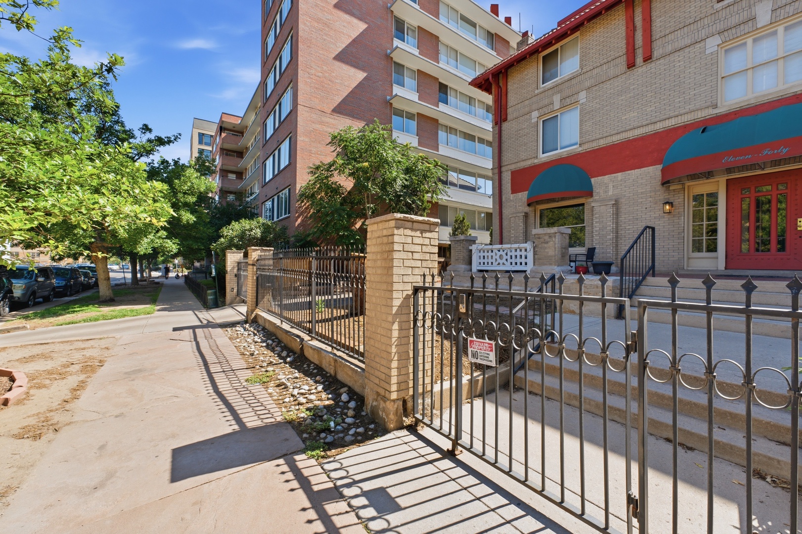 Property entrance situated in a quiet neighborhood with tree-lined streets, mid-rise residential buildings, and local shops nearby.