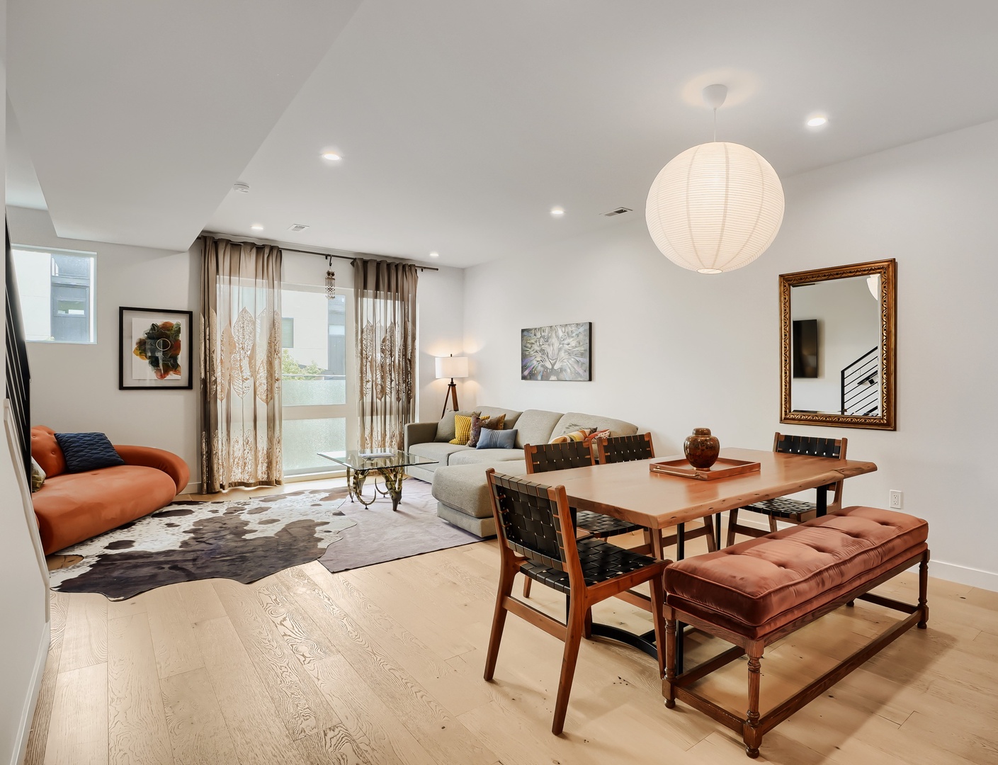 Step into your open-concept living space where natural light flows through airy curtains, casting warmth across light wood floors. Gather at the inviting dining table or sink into the plush seating—your perfect blend of style and comfort awaits.