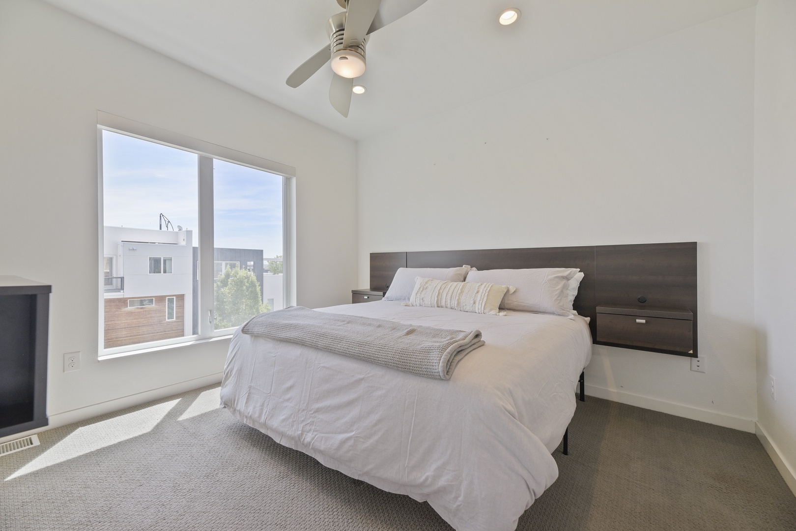 Rest easy in your serene bedroom, where plush bedding, vaulted ceilings with a ceiling fan, and abundant natural light create a peaceful retreat after exploring the city.