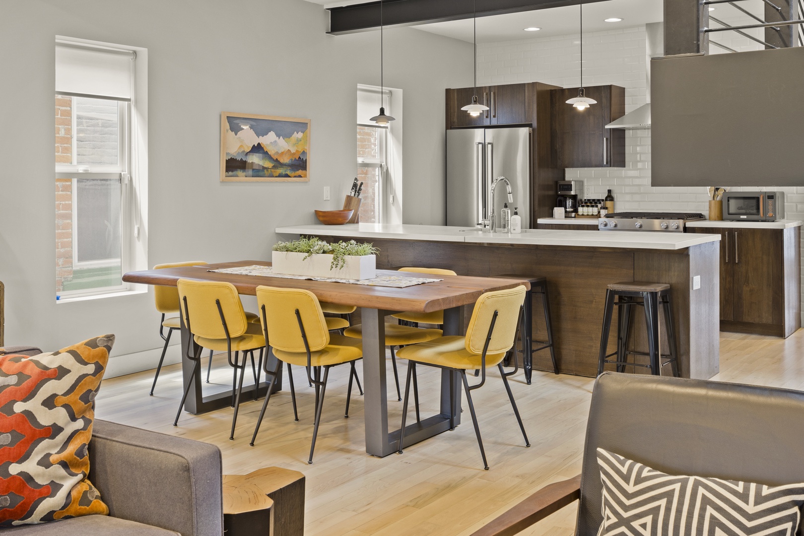 Your open-concept kitchen flows seamlessly into the dining area, where bright yellow chairs and warm wood create a cheerful space.