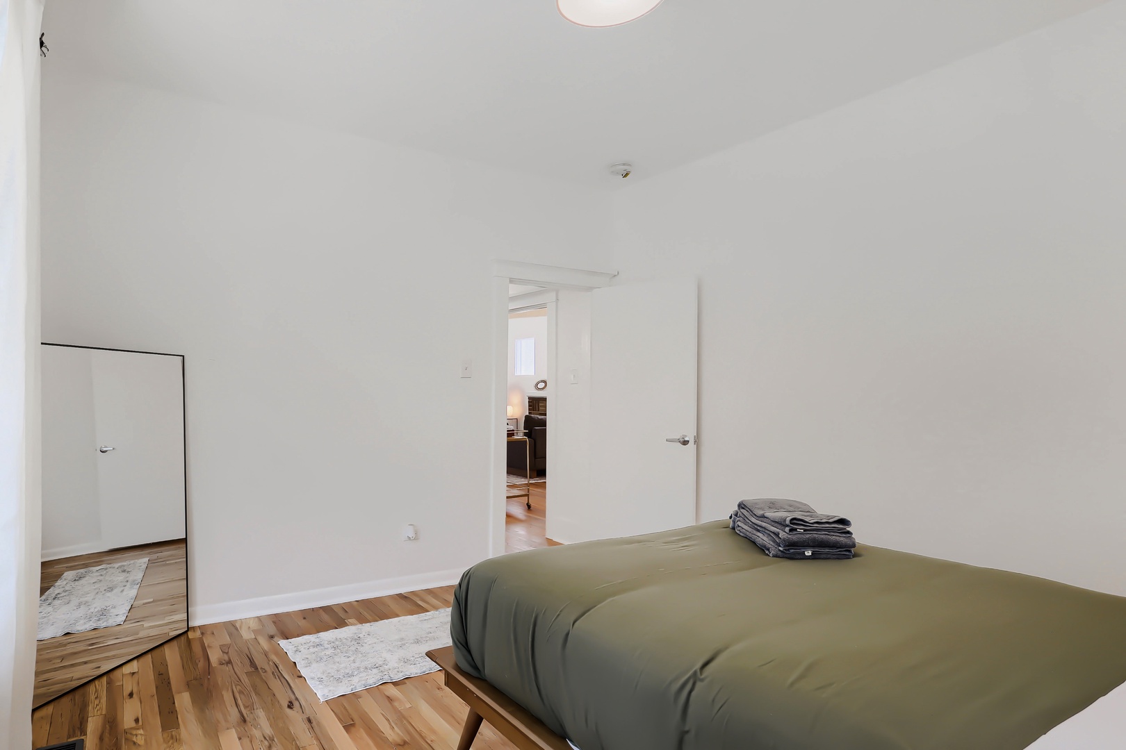 Your serene bedroom features warm wood floors, a comfortable bed with soft linens, and bright natural light from adjoining spaces, creating a peaceful retreat for restful nights.