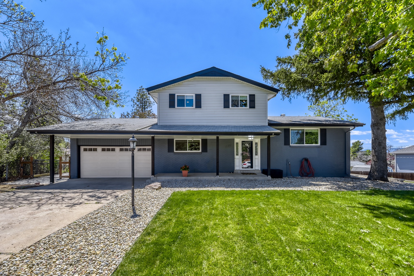 Two-story vacation rental with a manicured lawn and covered parking, set in a peaceful residential neighborhood with mature trees and clear blue skies.