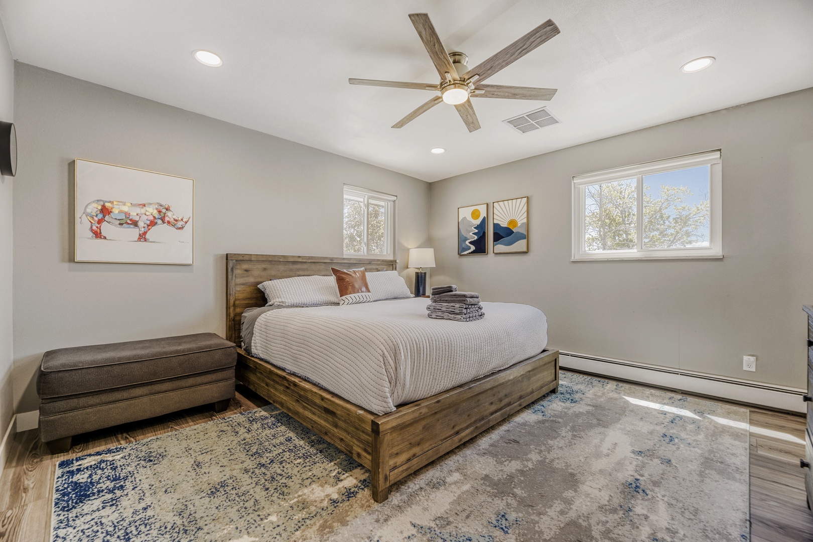 Your serene bedroom retreat features a plush queen bed, modern ceiling fan, and sunlit windows framing peaceful tree views—perfect for restful mornings and cozy evenings.