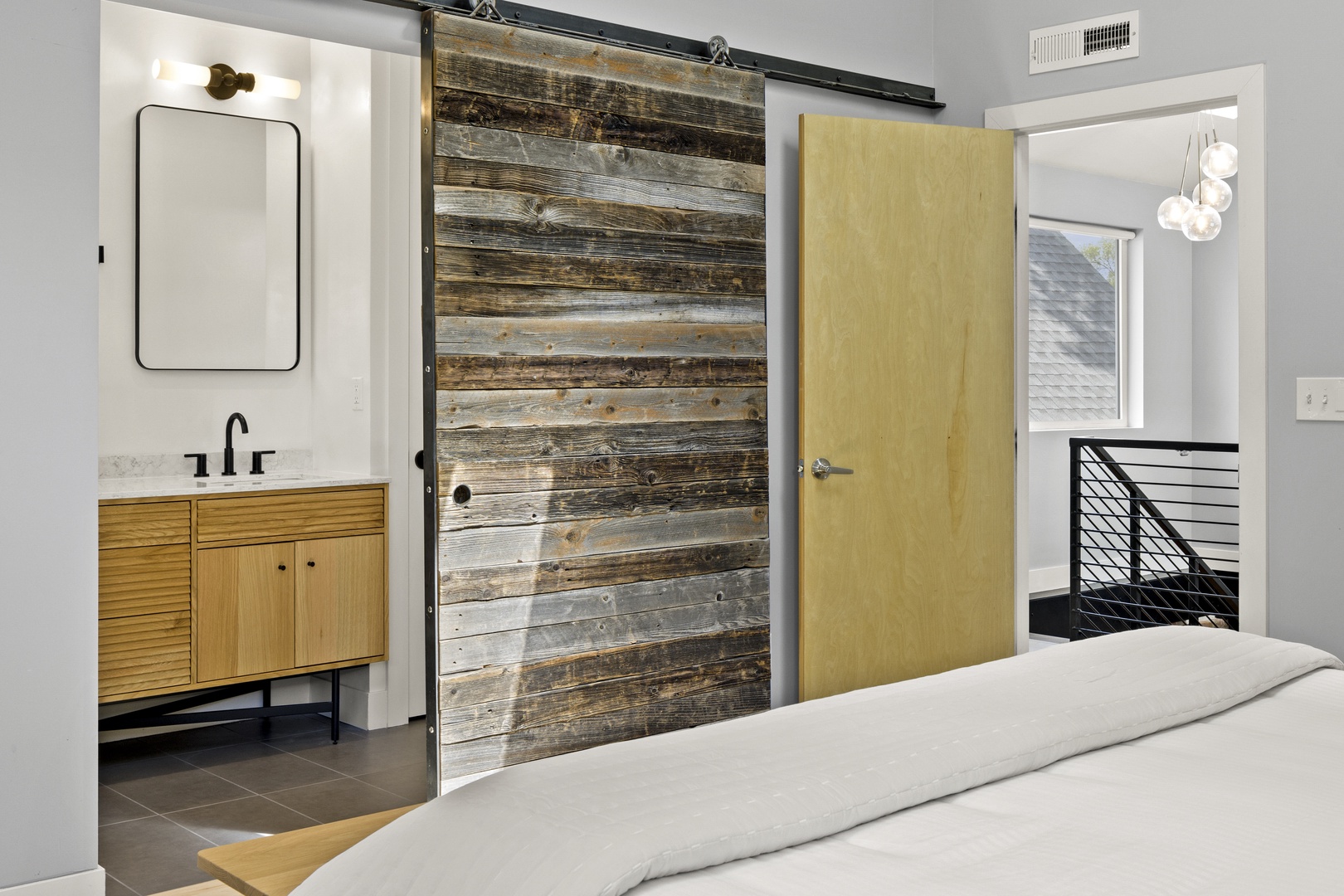 Your modern bedroom features stunning reclaimed wood barn doors and a sleek ensuite with warm wood vanity details.